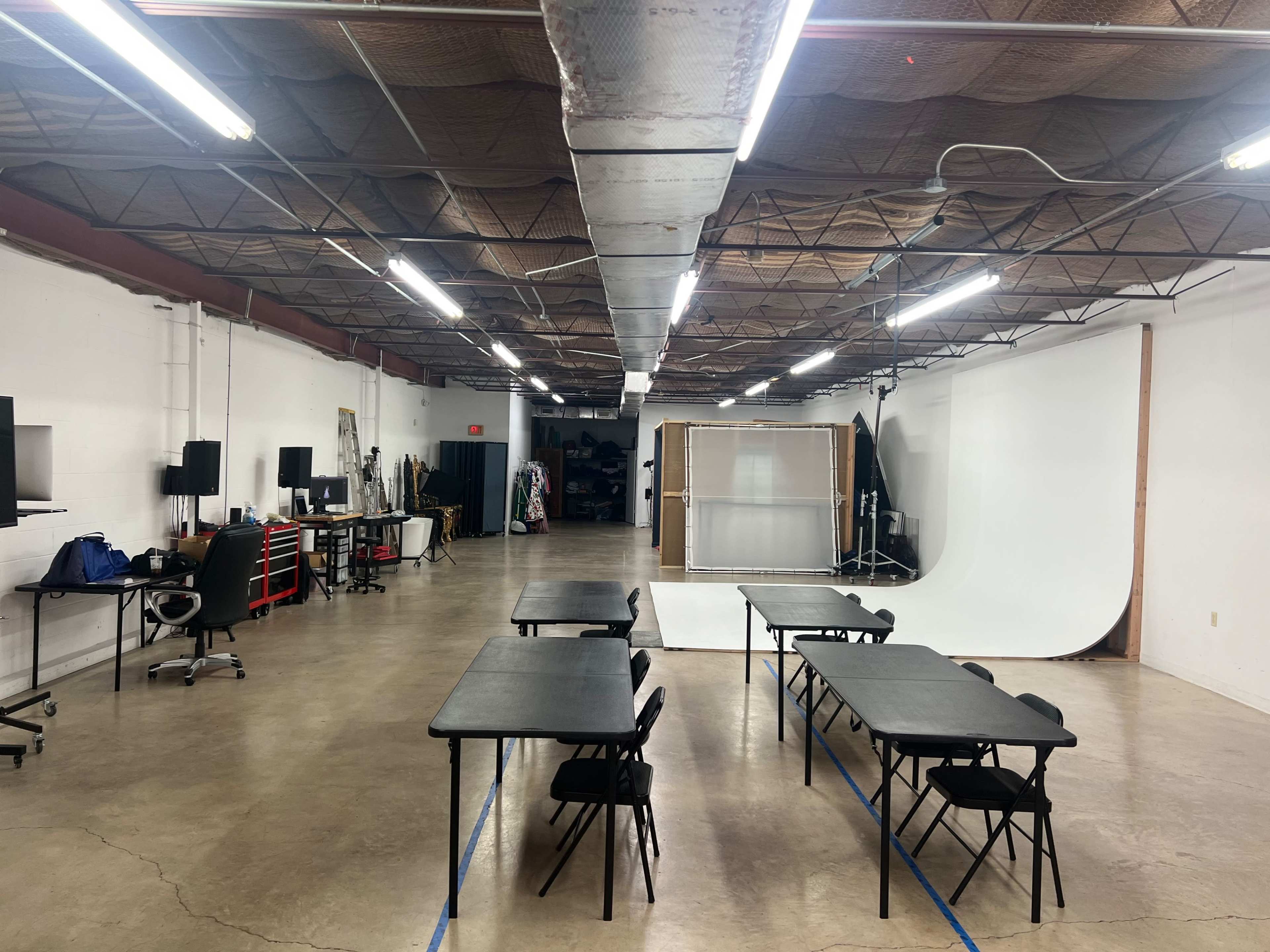 A spacious, well-lit studio with several tables and chairs arranged in the foreground and a white backdrop set up in the background.