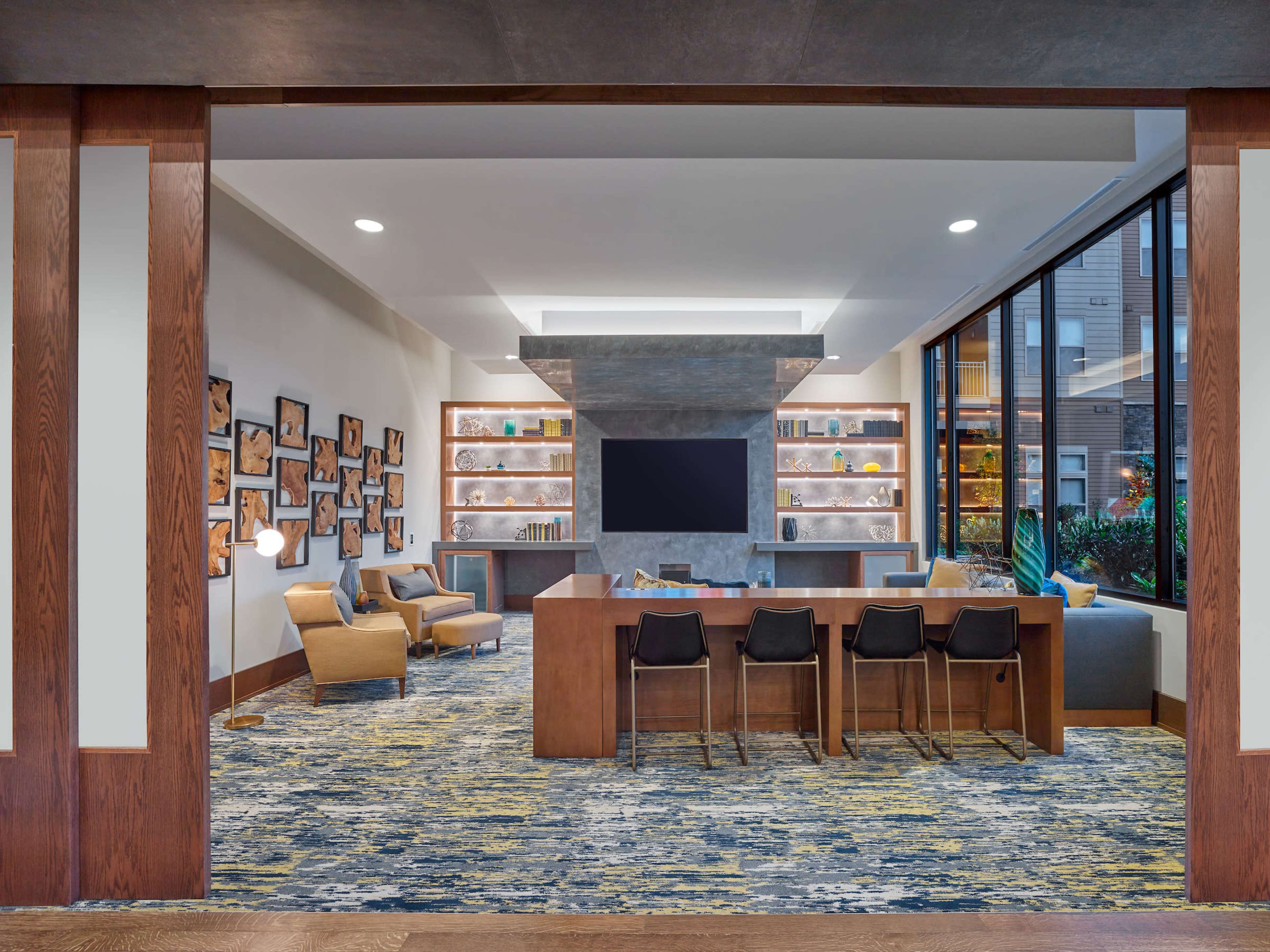 A modern lobby area featuring seating, shelves with decorative items, a large television, and large windows allowing natural light.