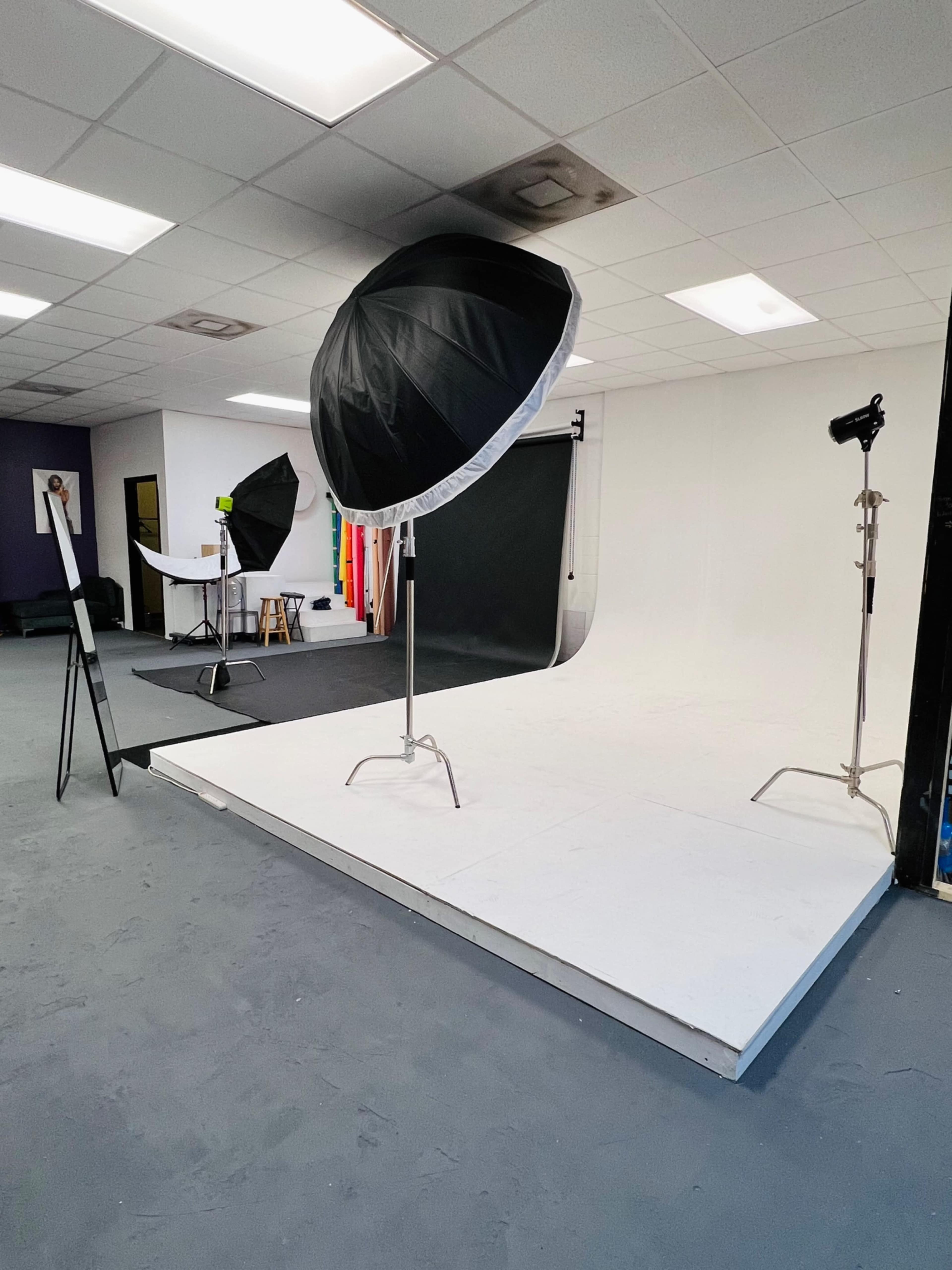 A photography studio setup with lighting equipment, backdrops, and a raised white platform.