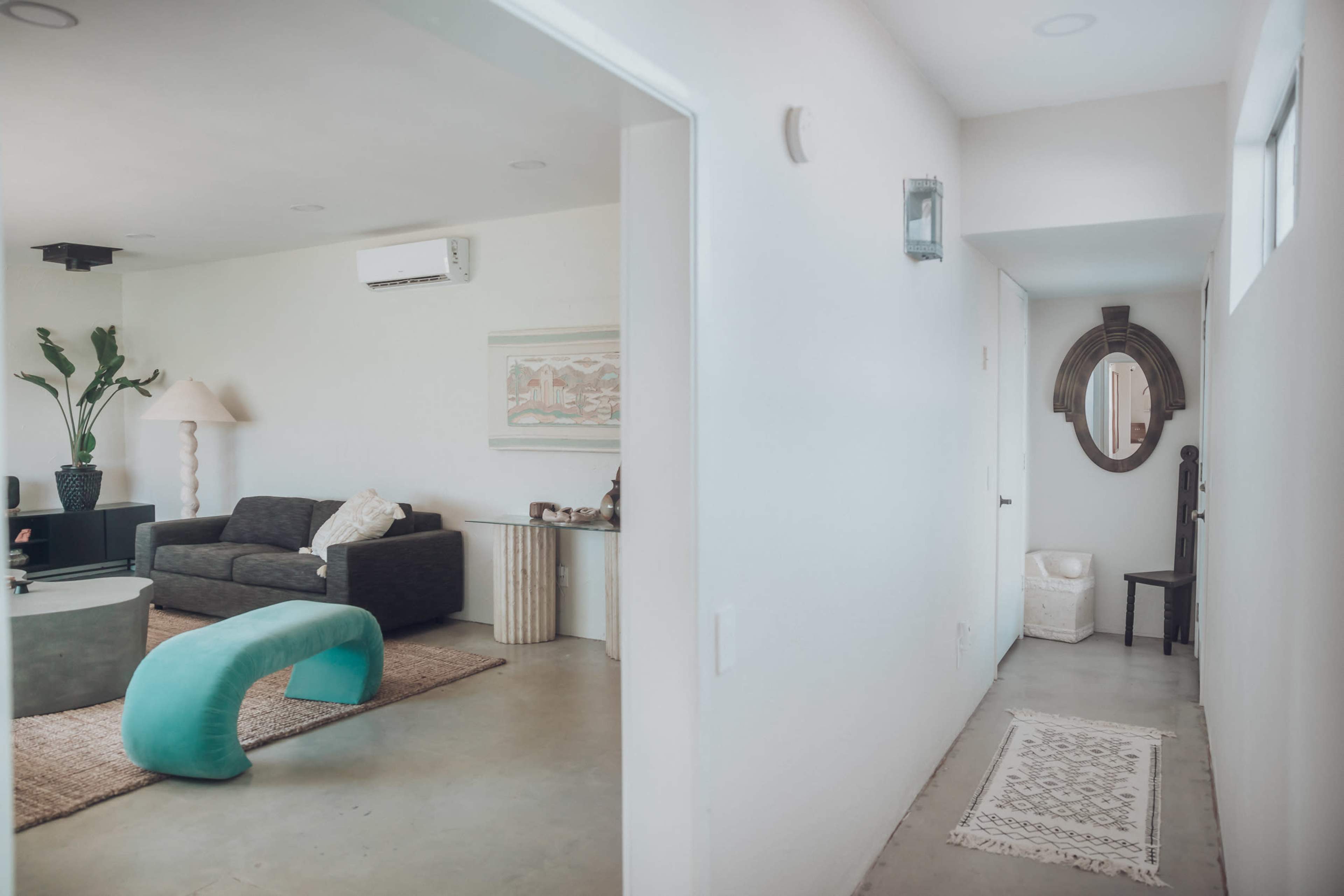 A spacious, modern living area leads to a hallway featuring a mirror and a chair.