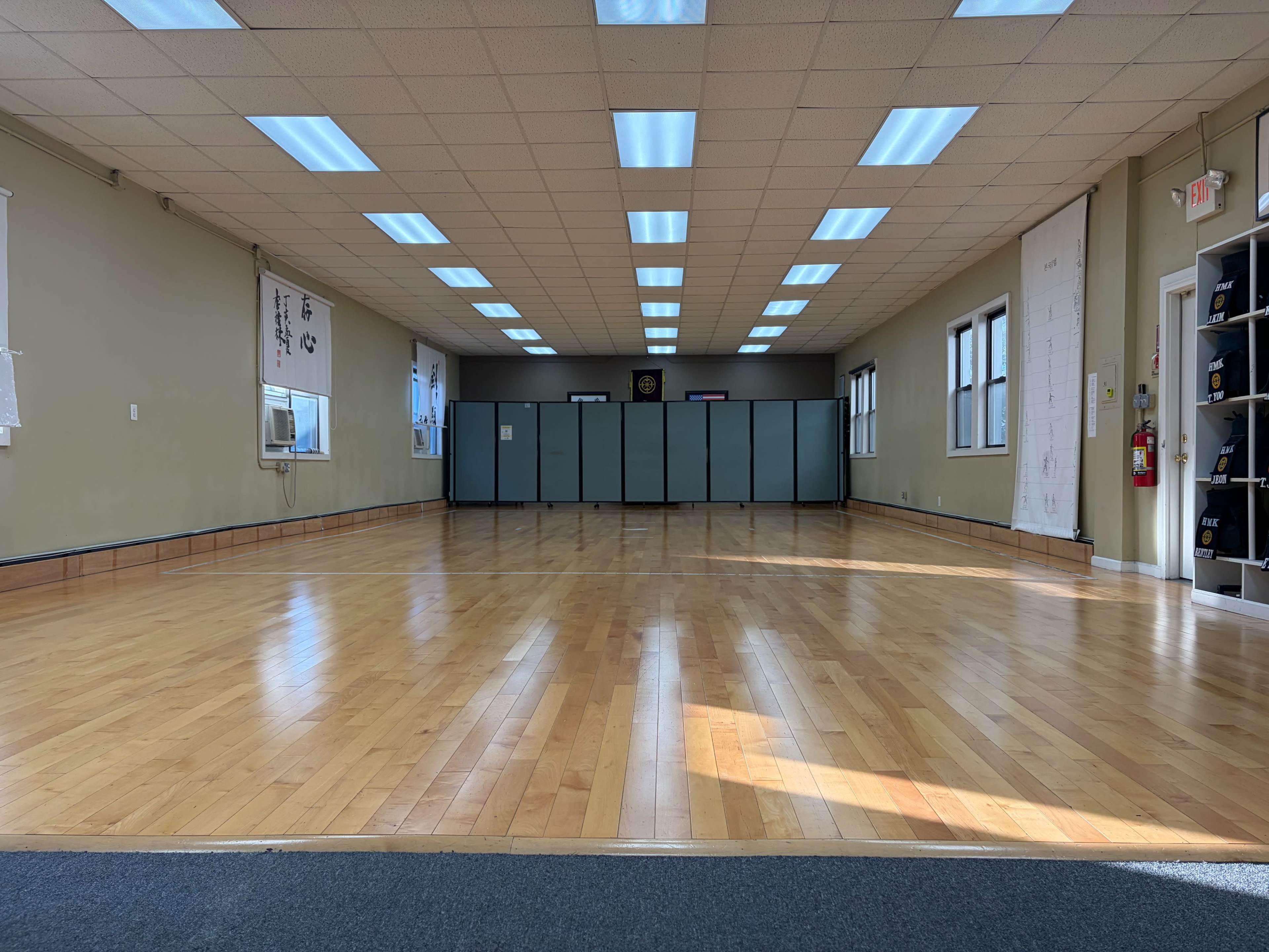 The image shows a spacious, empty wooden floor room with large windows and simple wall decorations.