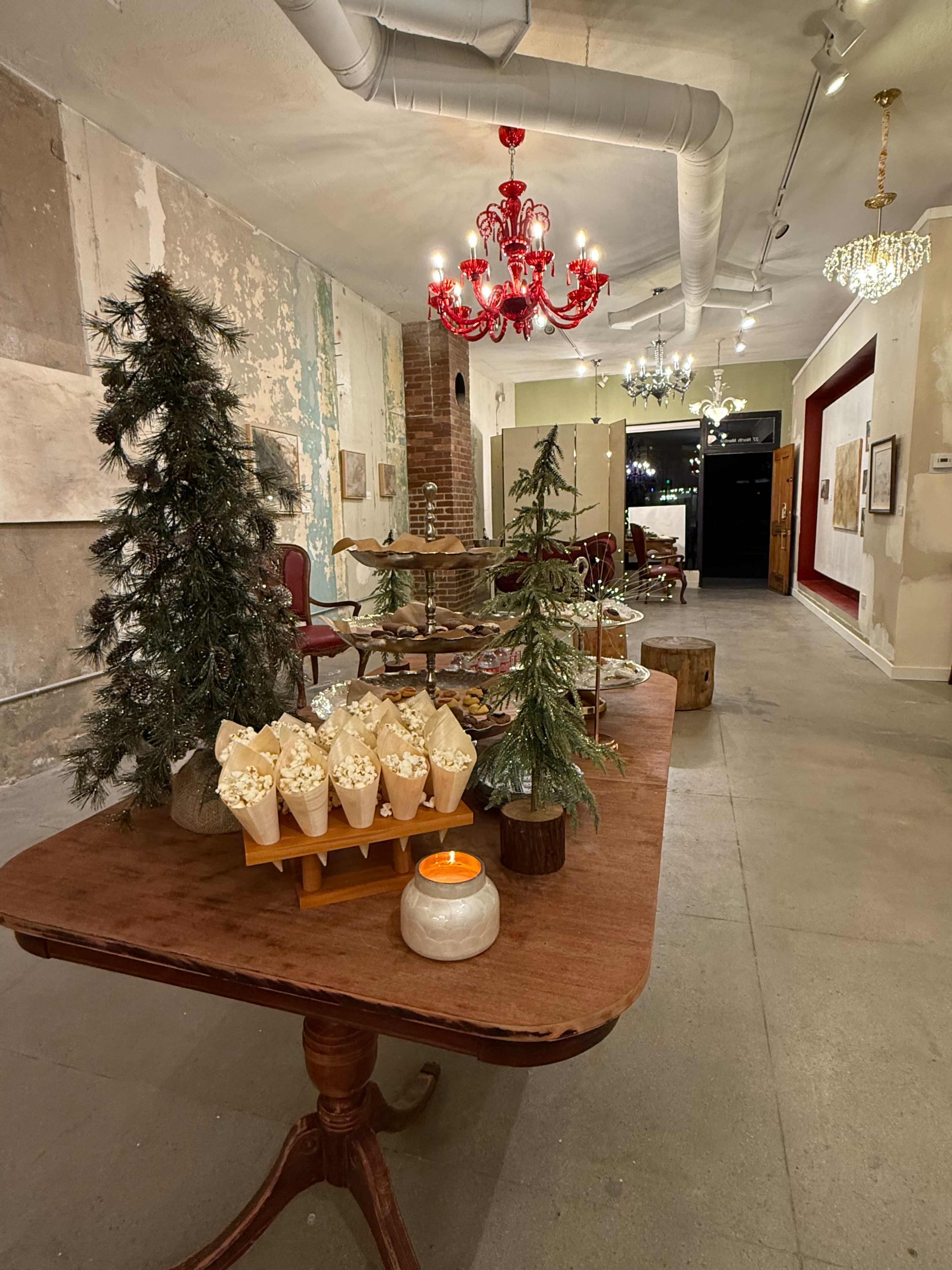 The image shows a decorated interior space featuring a wooden table with popcorn cones, small Christmas trees, and various lighting fixtures such as chandeliers and a red lamp.