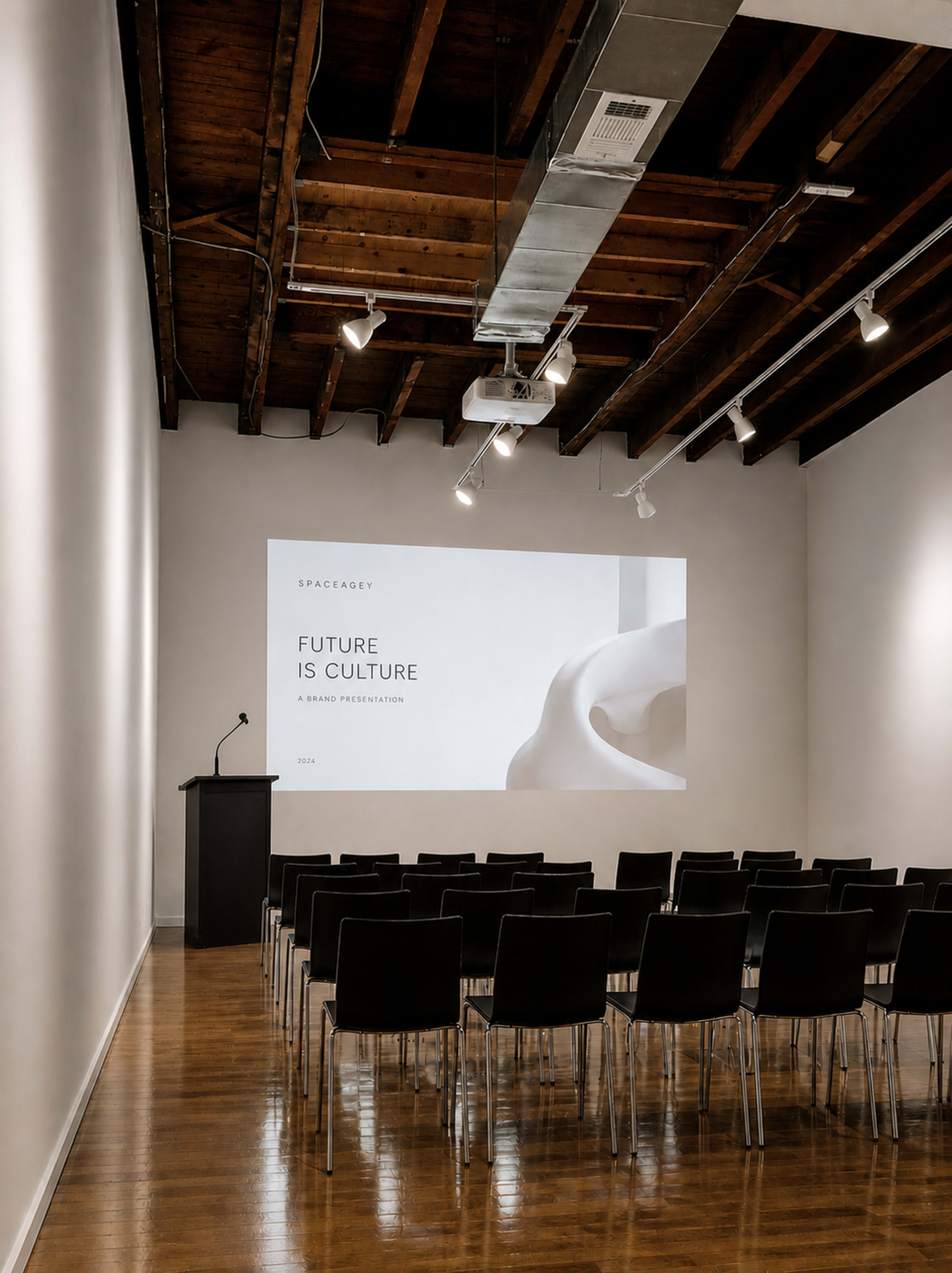 A minimalist gallery space features rows of black chairs facing a projection that reads "FUTURE IS CULTURE" against a white wall.