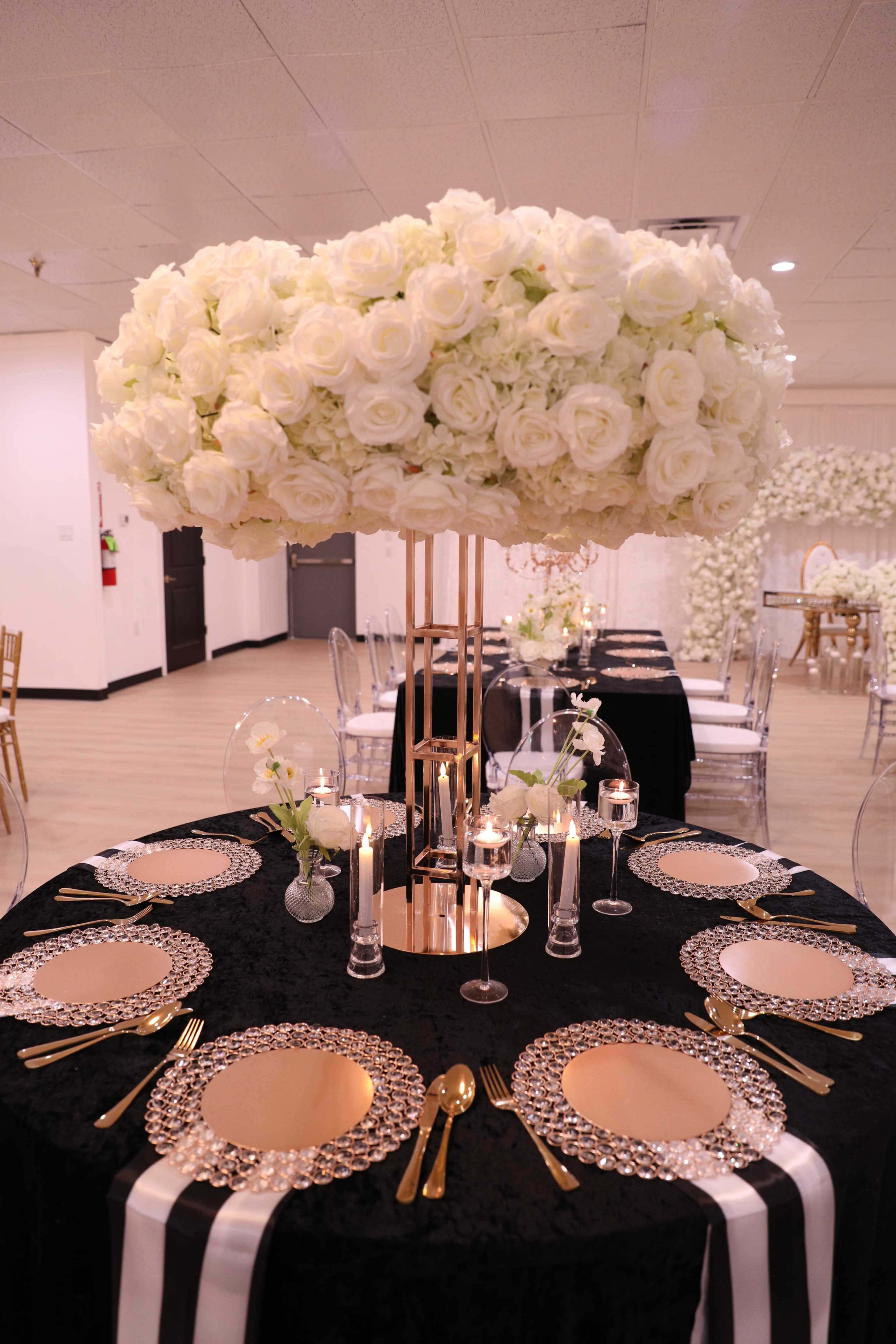 A large arrangement of white roses is positioned atop a black table with gold accents, set for a formal dining experience.