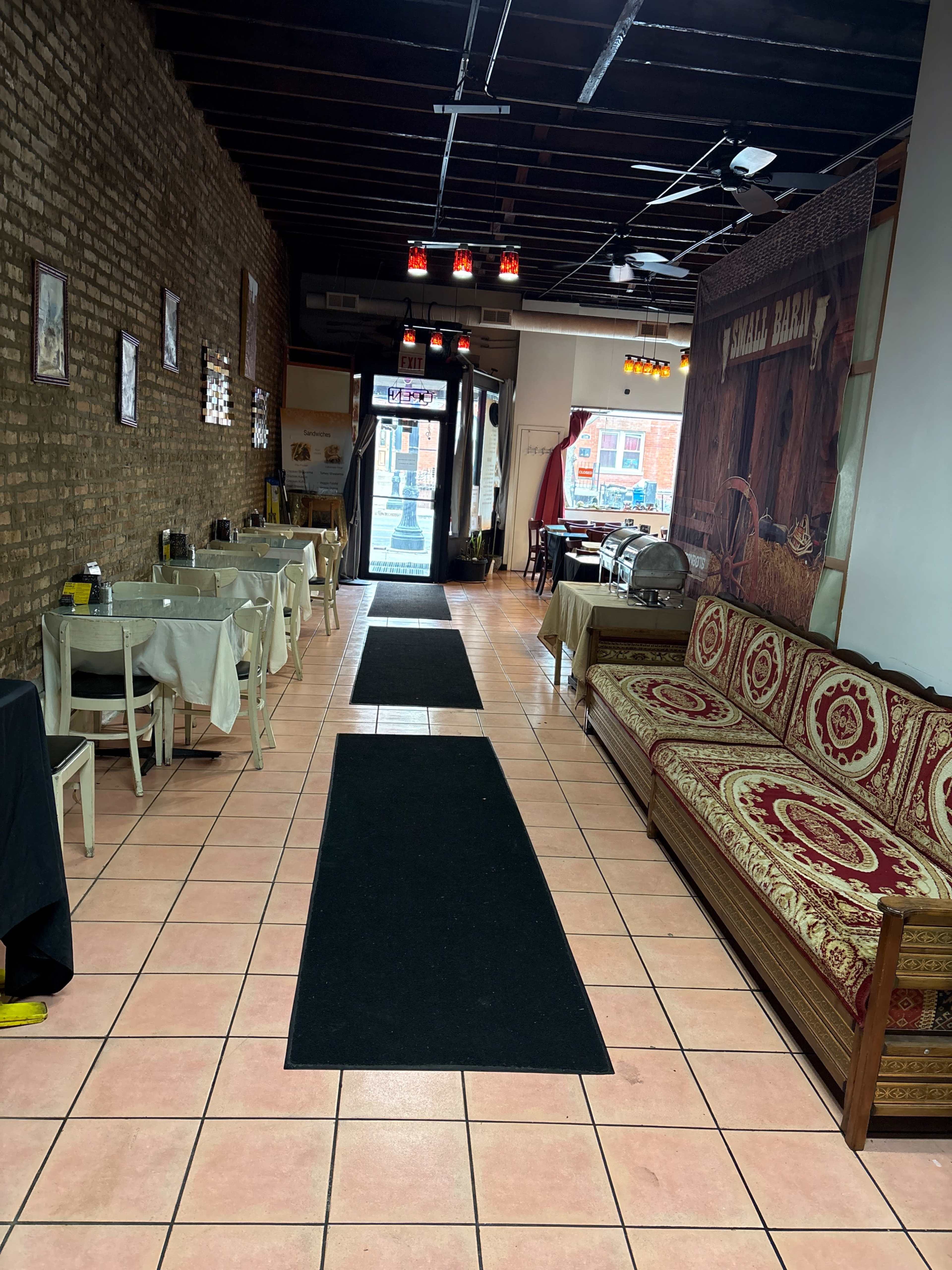 The image shows a narrow restaurant interior with tiled floors, a long brown carpet running down the center, and tables on either side.
