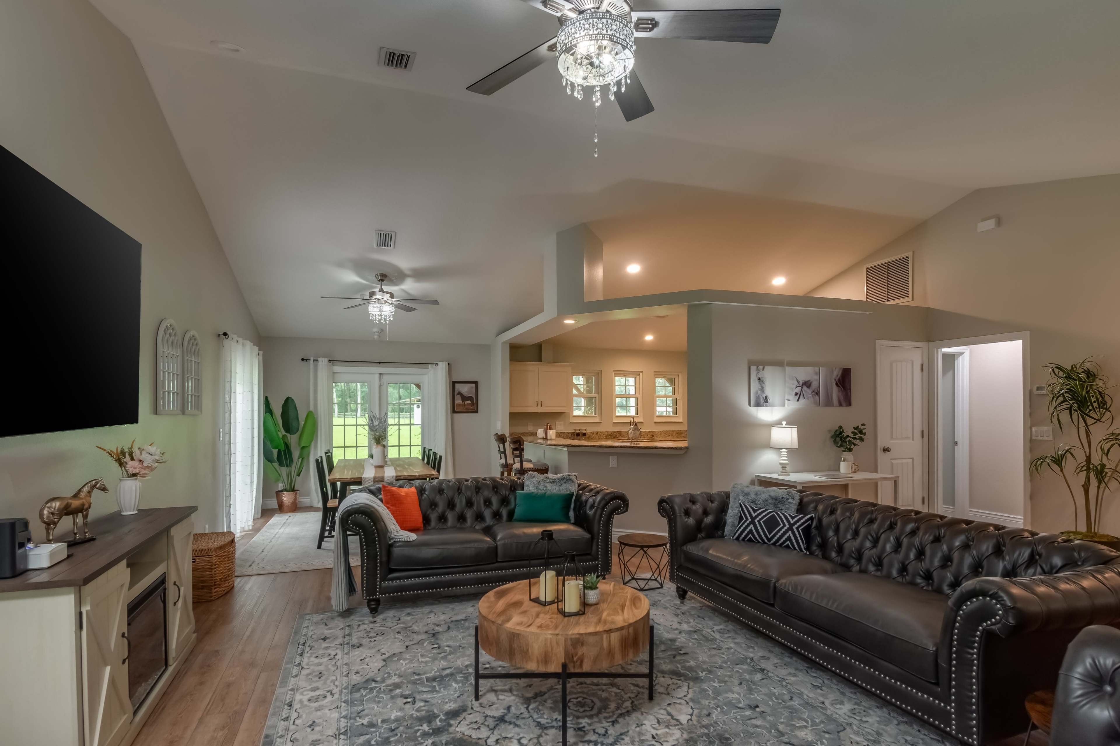 A spacious living room features two leather sofas, a wooden coffee table, and a view into the kitchen area.