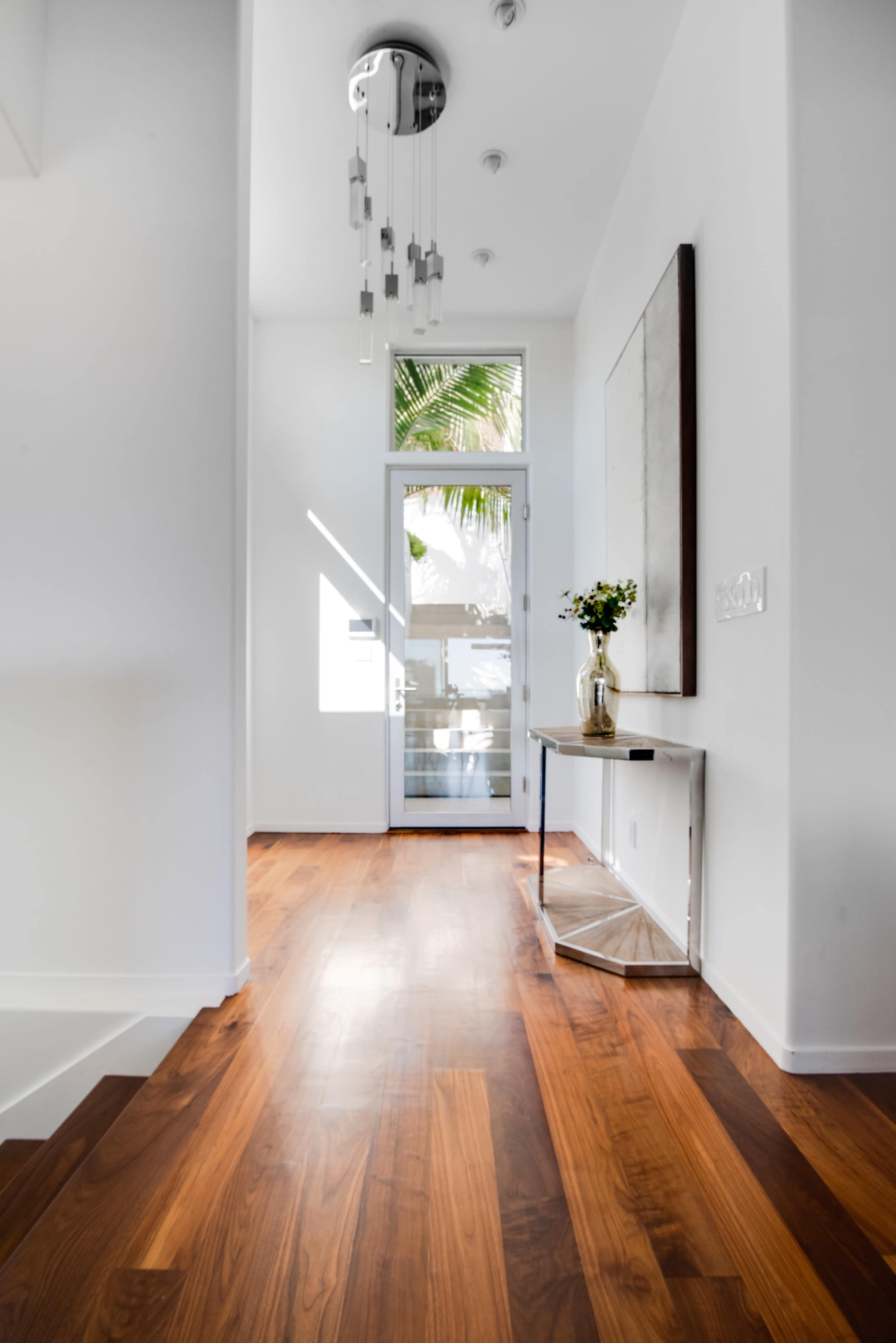 A bright hallway with wooden flooring, a small console table, and a door leading to an outdoor area.
