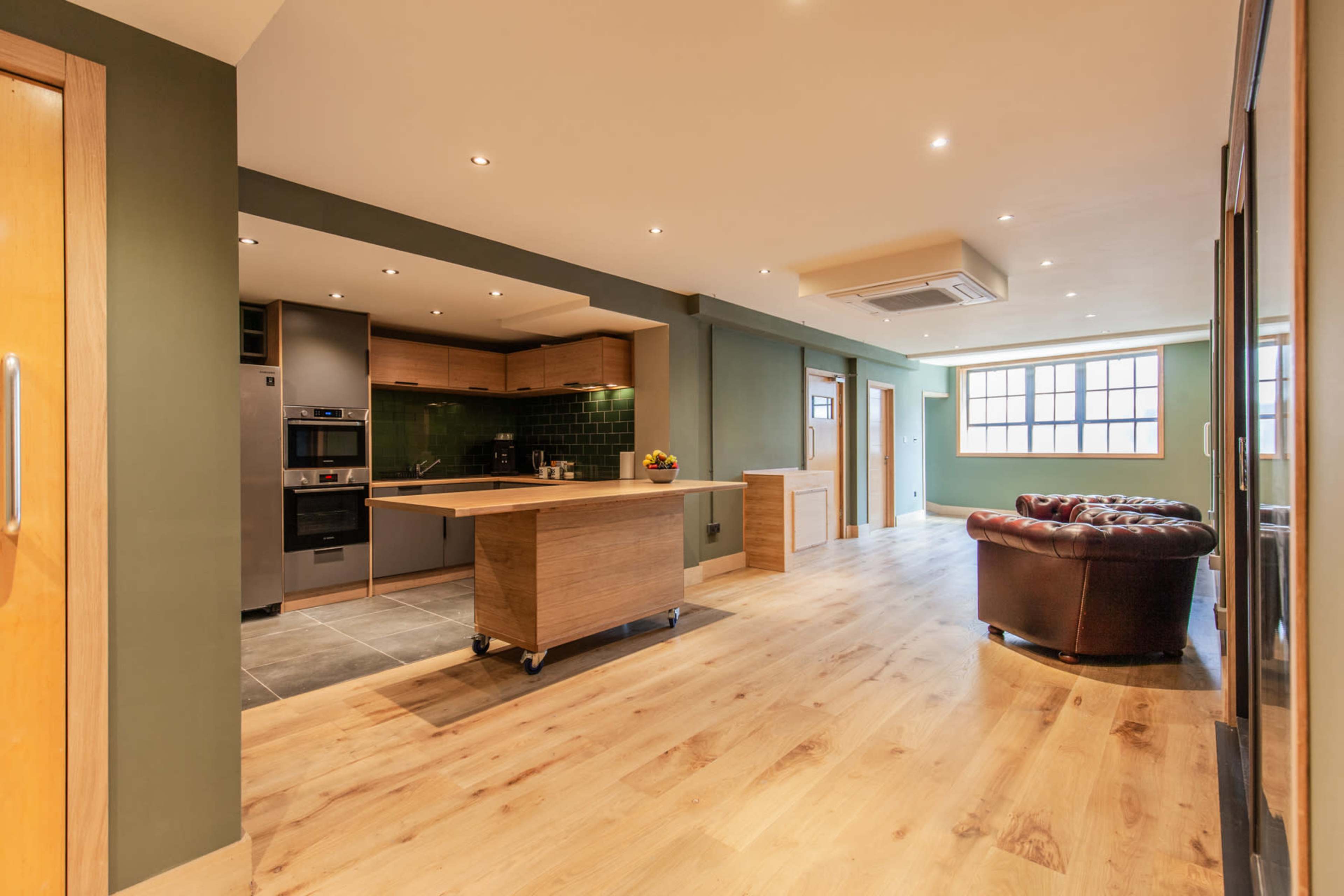 A spacious open-plan kitchen and living area with a wooden floor, modern cabinetry, and a leather seating arrangement.