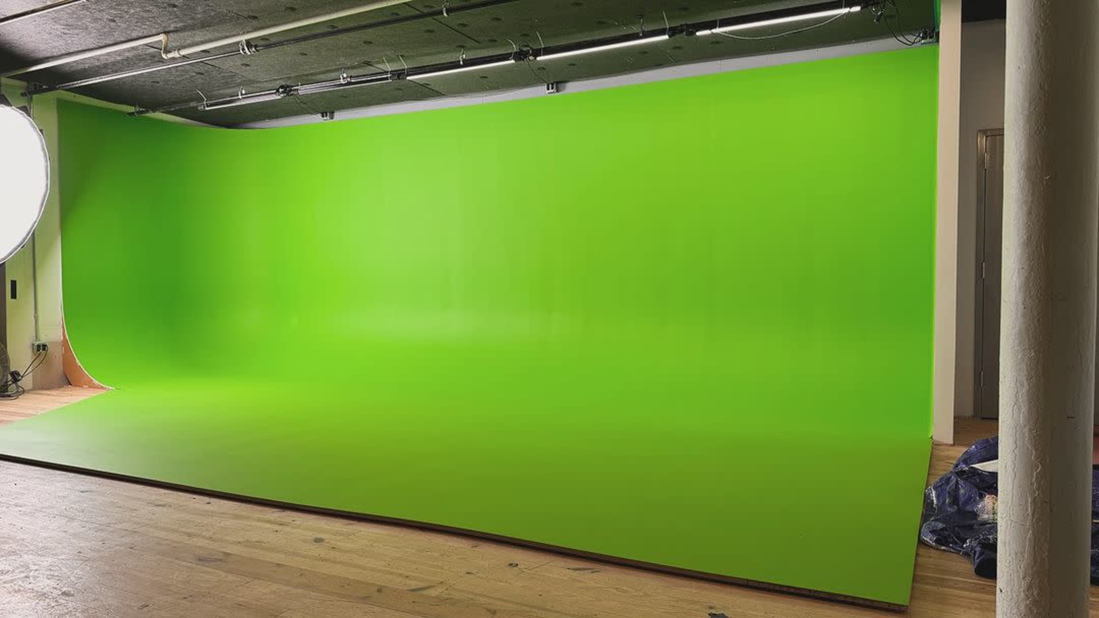 The image shows a bright green studio backdrop in an empty room with wooden flooring.