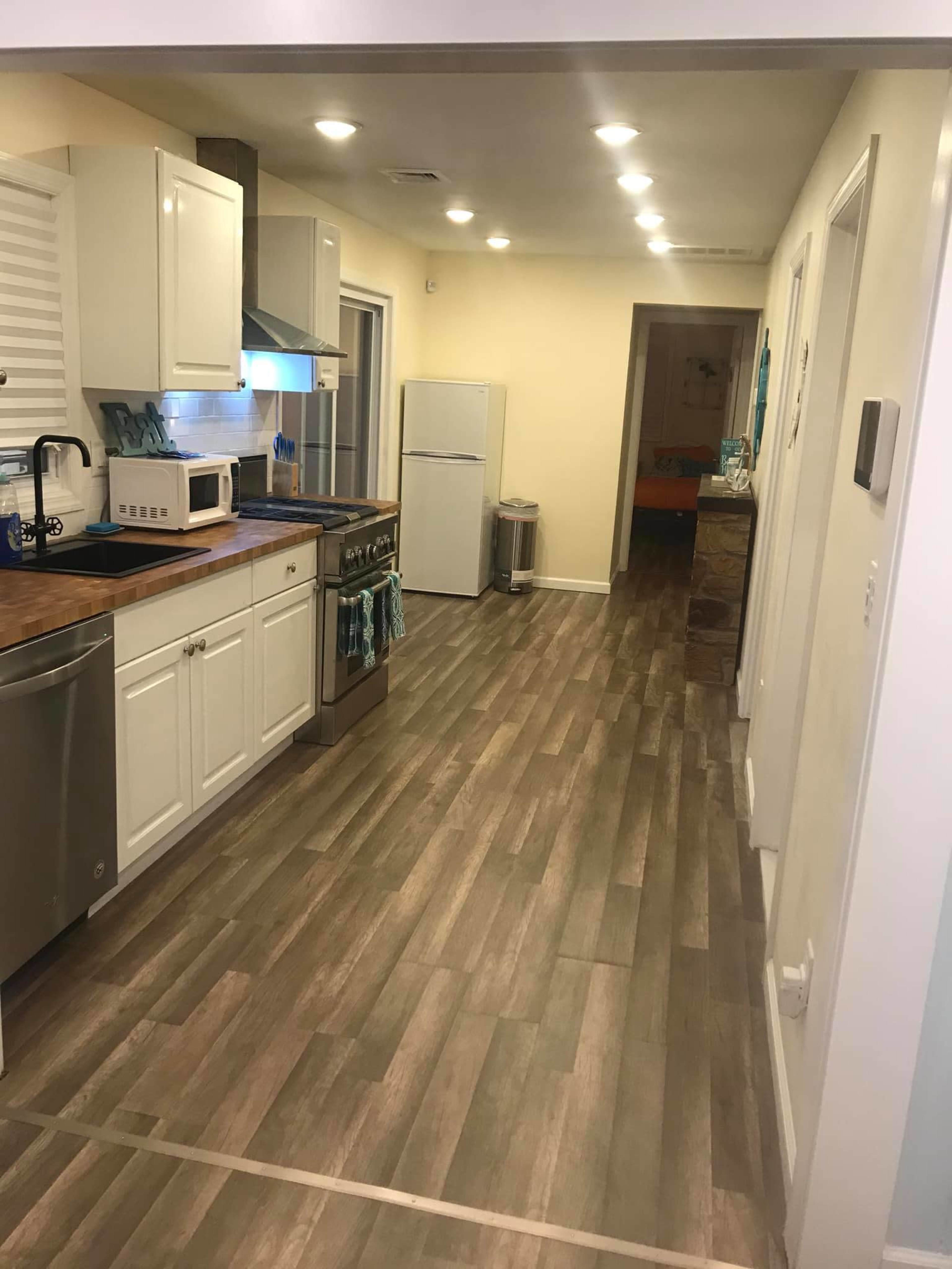 A modern kitchen with white cabinets, a stainless steel refrigerator, and a long corridor leading to a partially visible hallway.