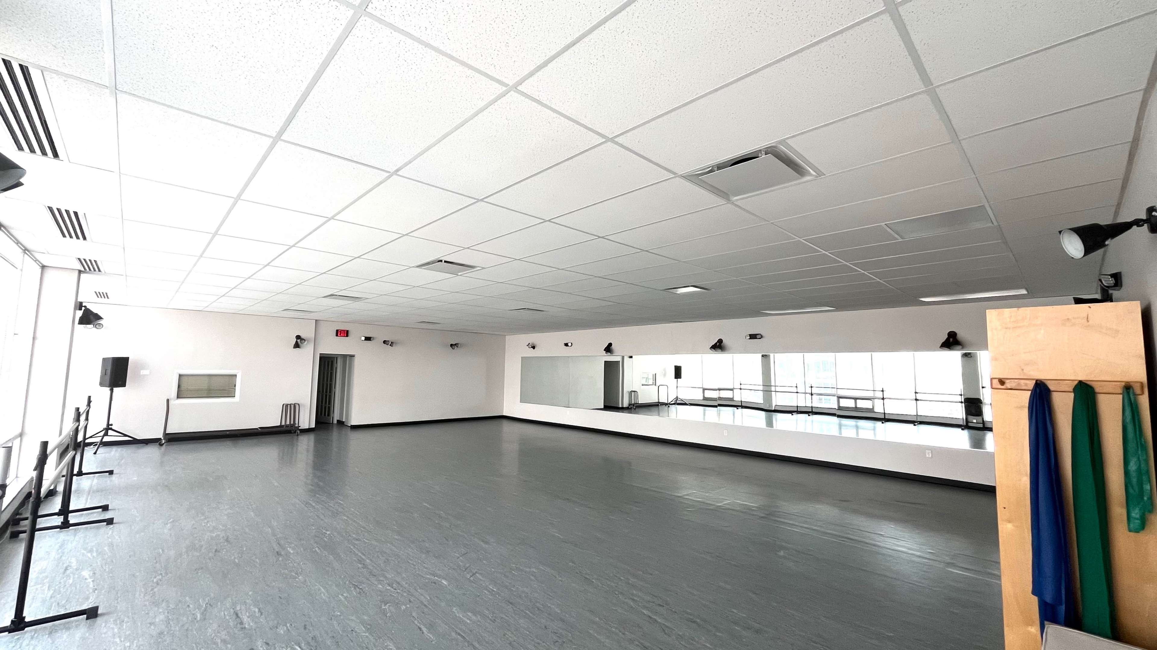 A spacious dance studio features a smooth wooden floor, large mirrors, and wall-mounted lights.