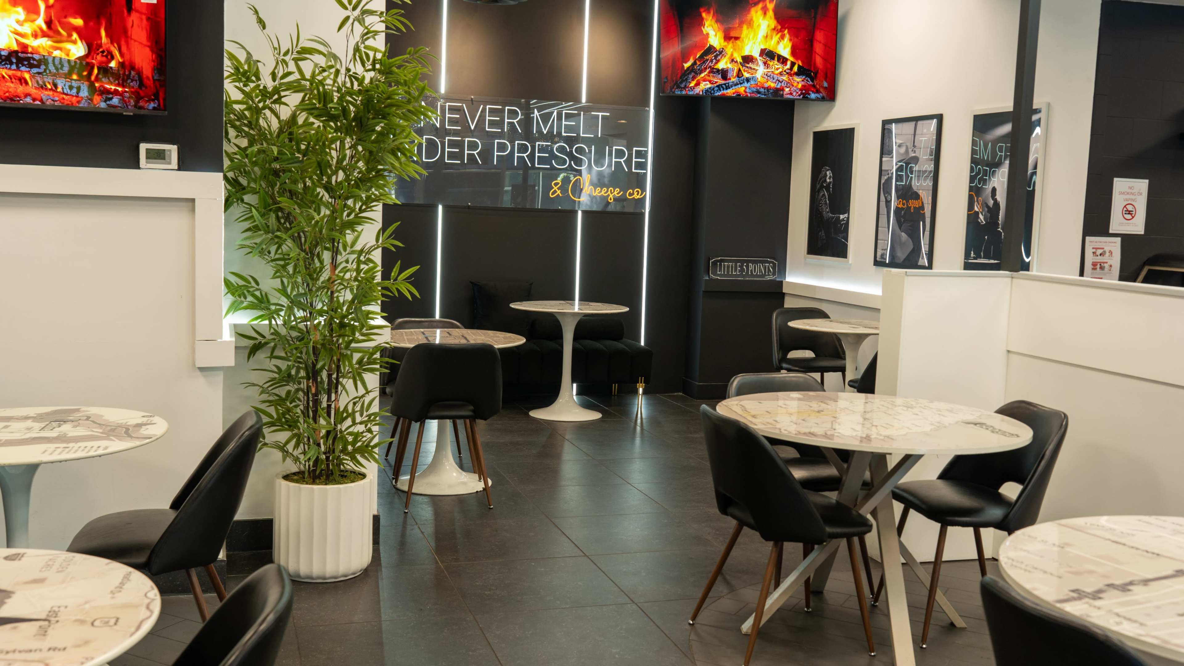 The image shows a modern cafe interior with several white tables and chairs, a potted plant, and walls adorned with black-and-white photographs.