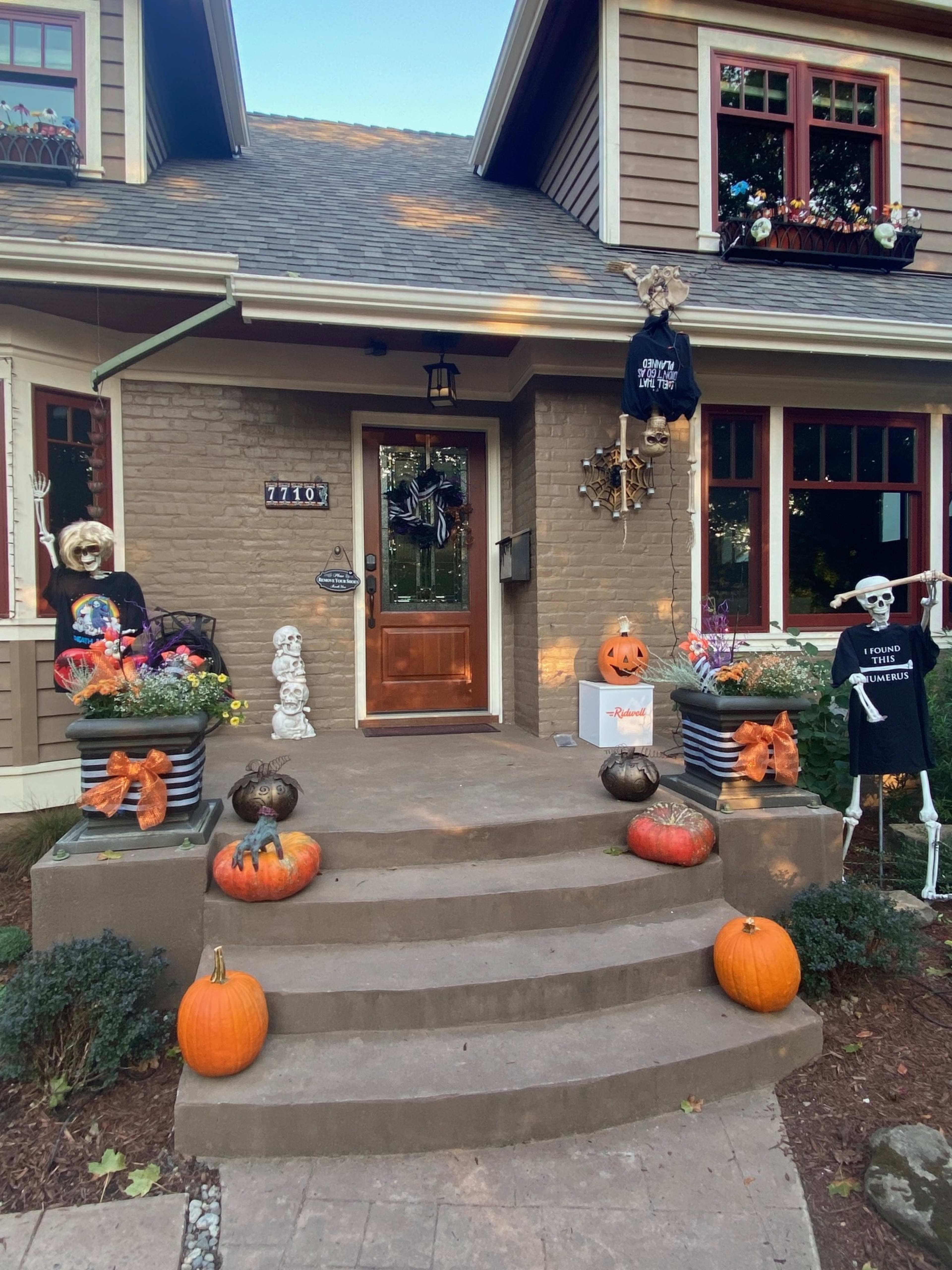 A house decorated for Halloween features a front porch with pumpkins, skeletons, and festive ornaments.