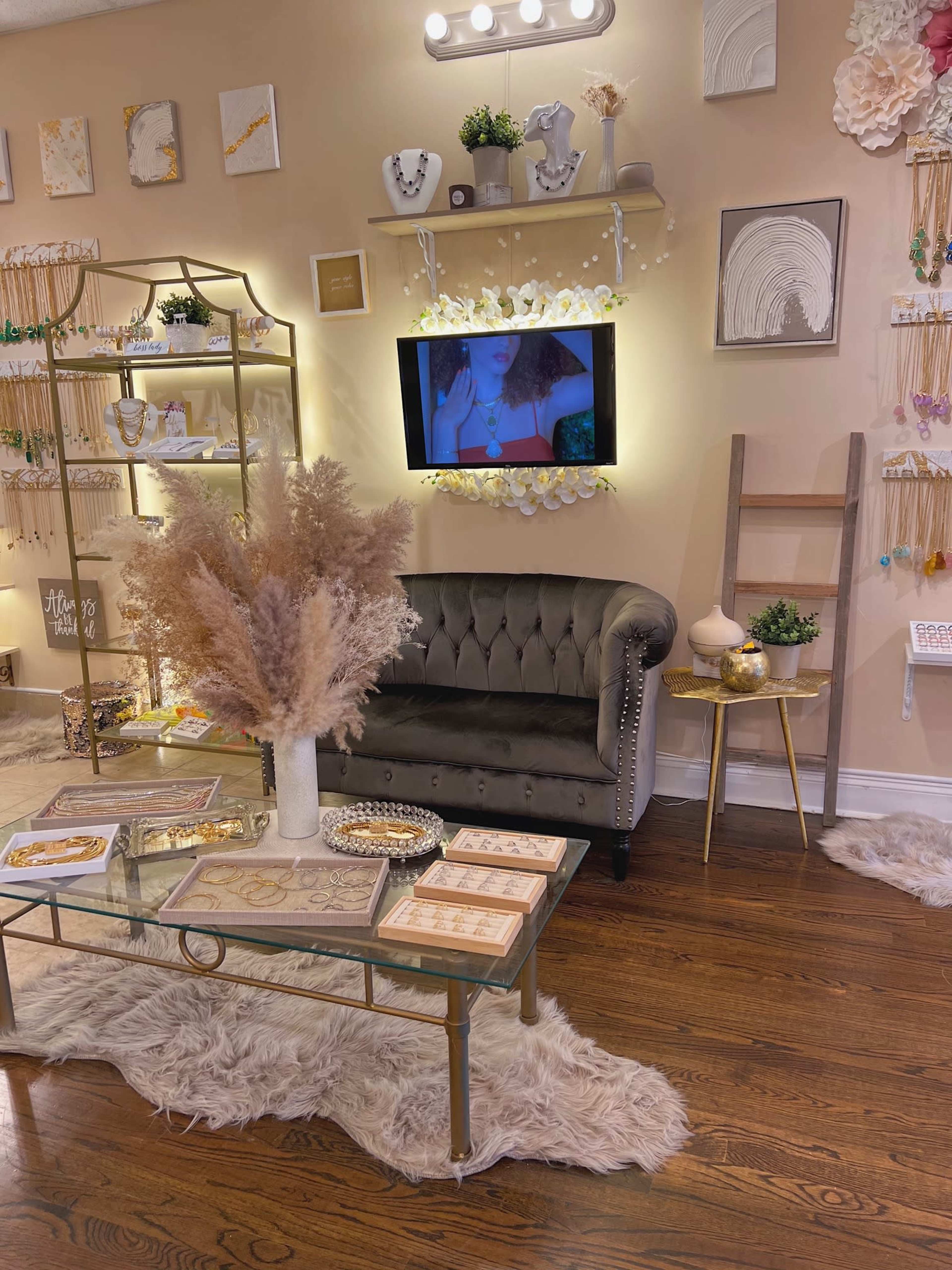 A boutique interior featuring a velvet sofa, a glass coffee table, decorative wall displays, and a television playing a video.