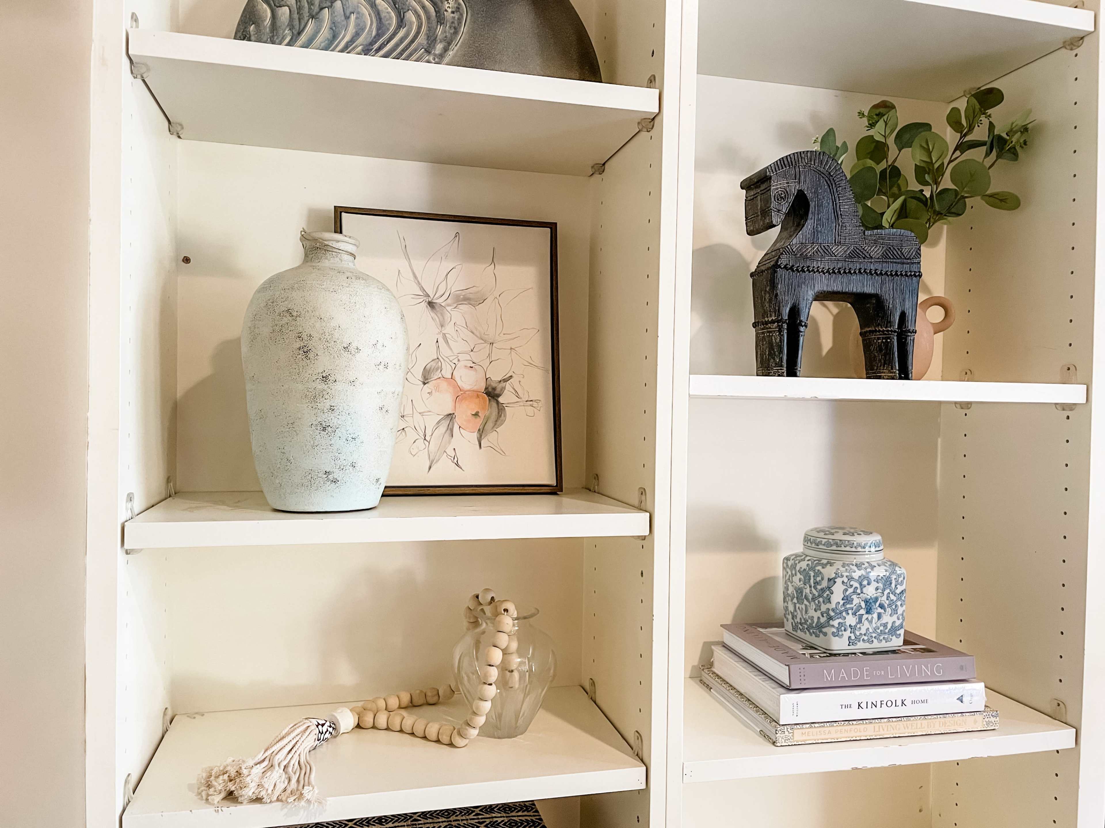 A white shelving unit with decorative items, including a vase, a framed artwork, a small horse figurine, and stacked books.