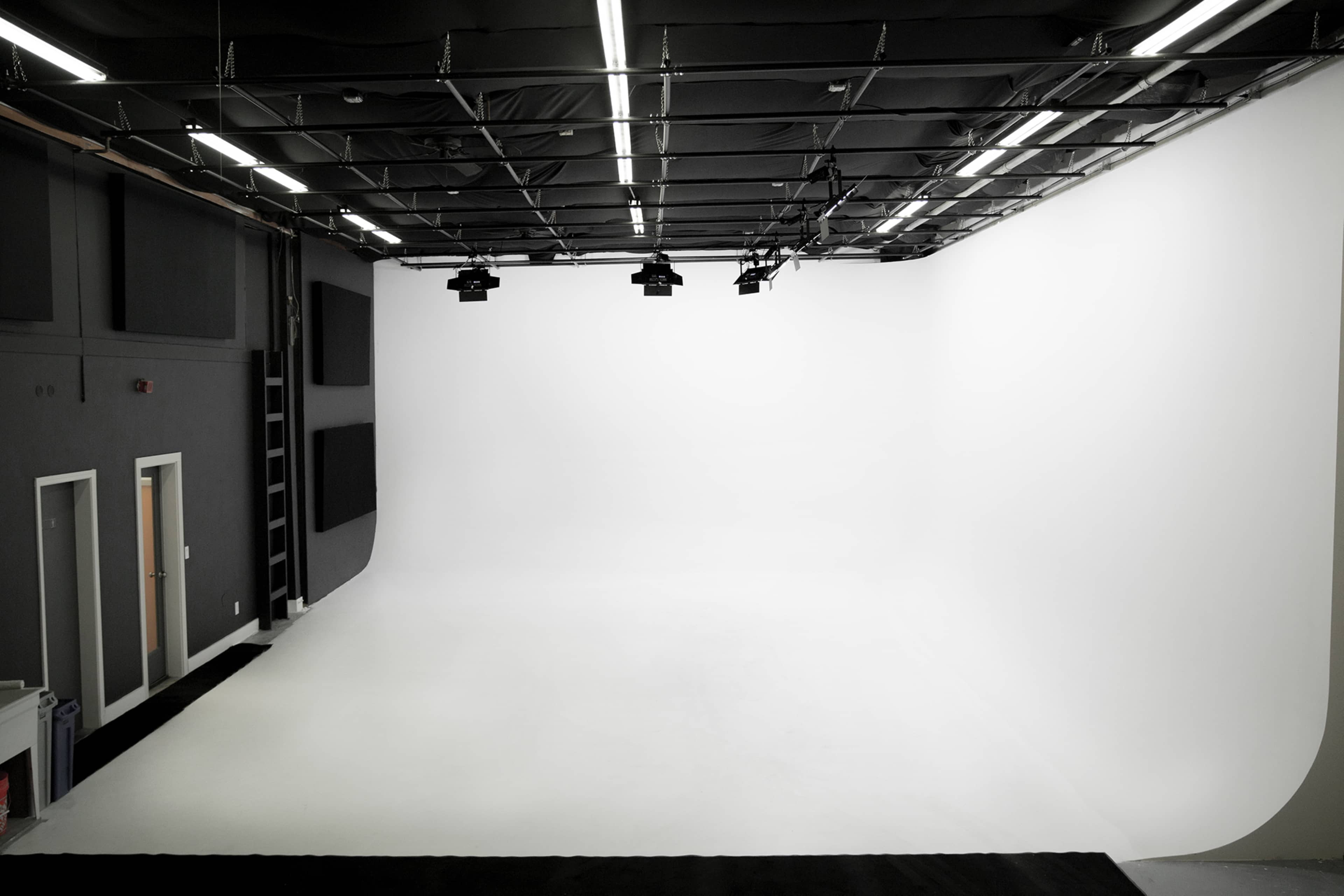 The image shows a spacious photography studio with a seamless white backdrop and overhead lighting.