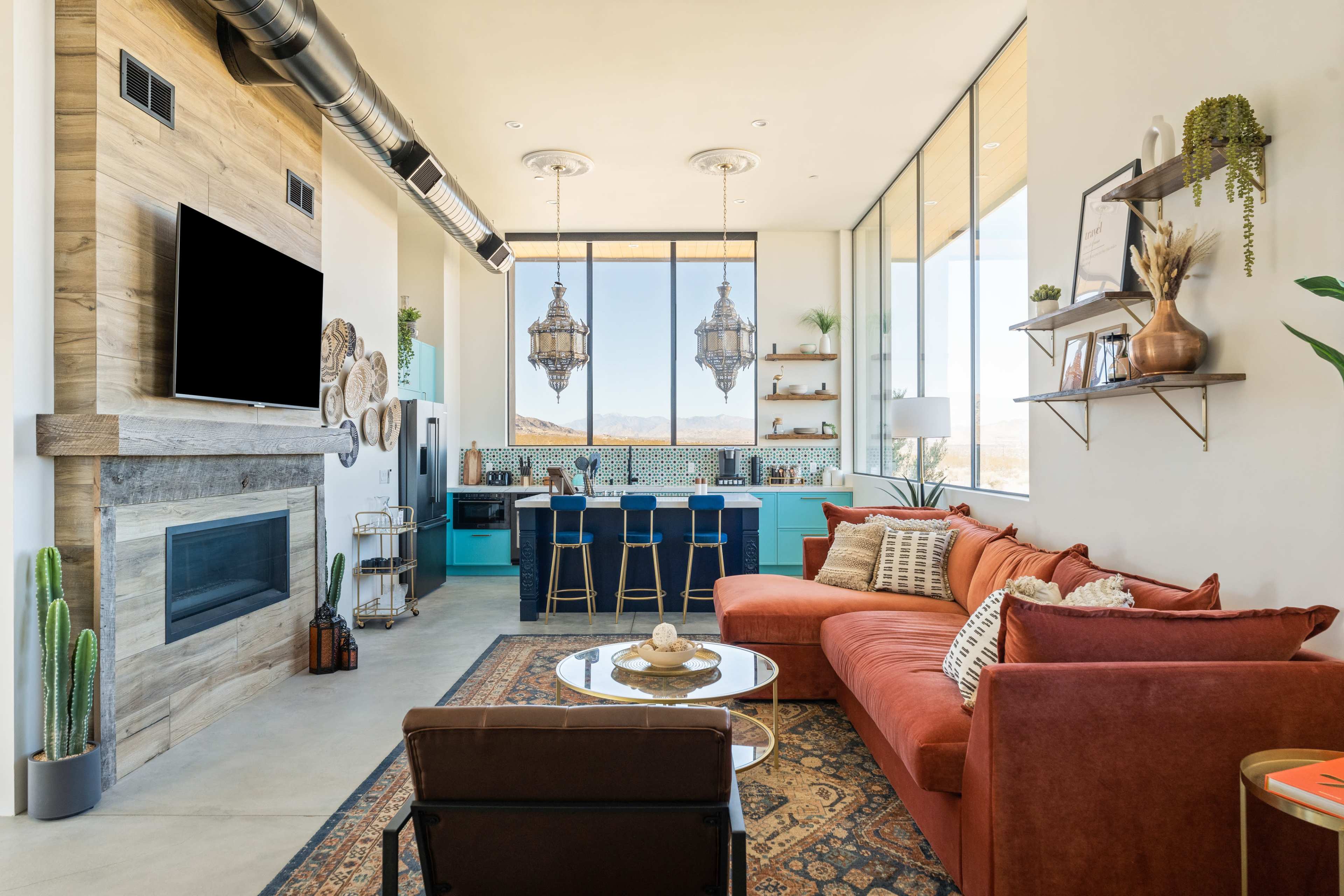 The image shows a modern living room with a red sofa, a low coffee table, and an adjoining kitchen featuring turquoise cabinetry and pendant lights.