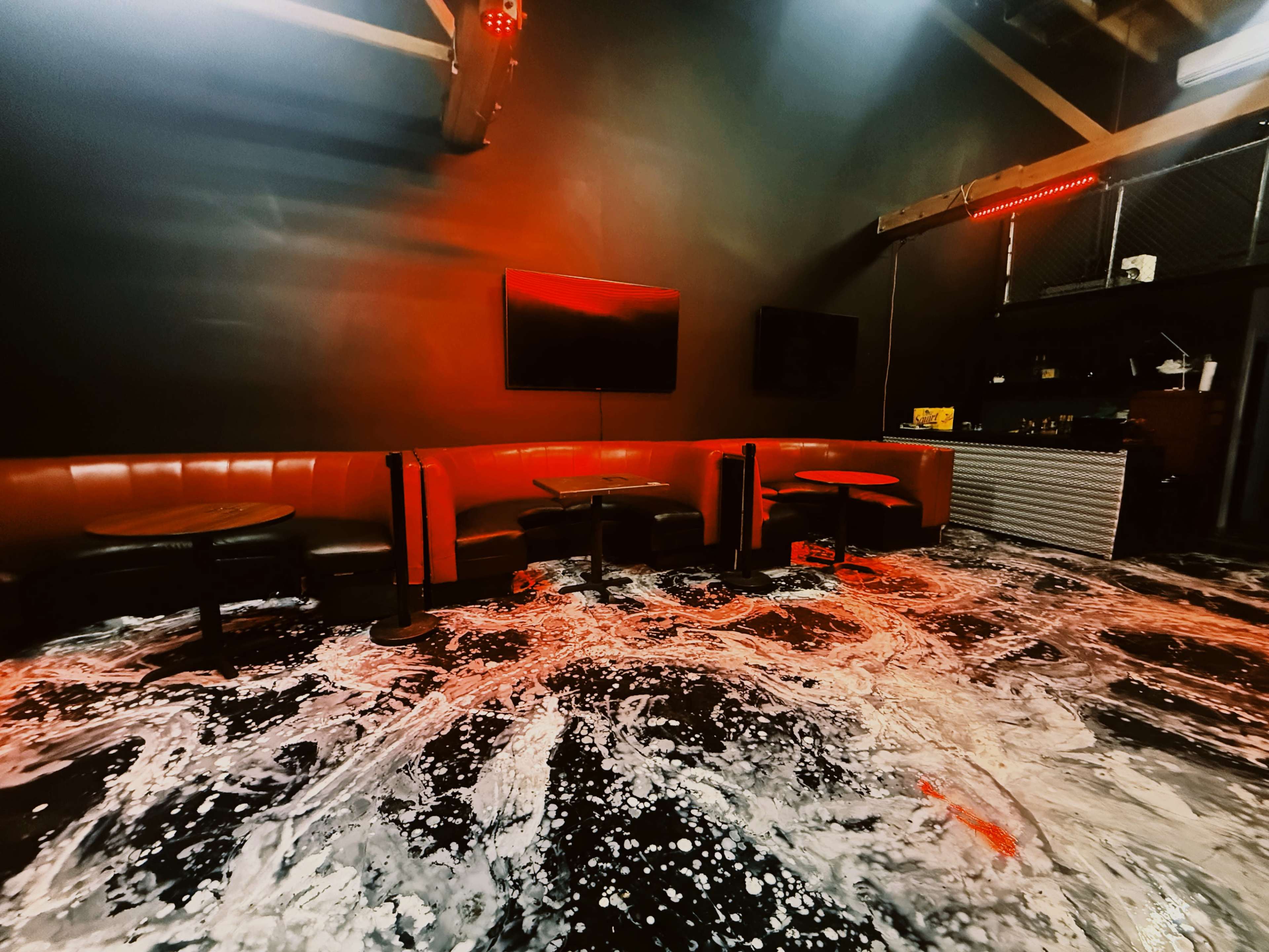 The image shows a dimly lit room with red lighting, featuring booth seating and scattered foam or liquid covering the floor.