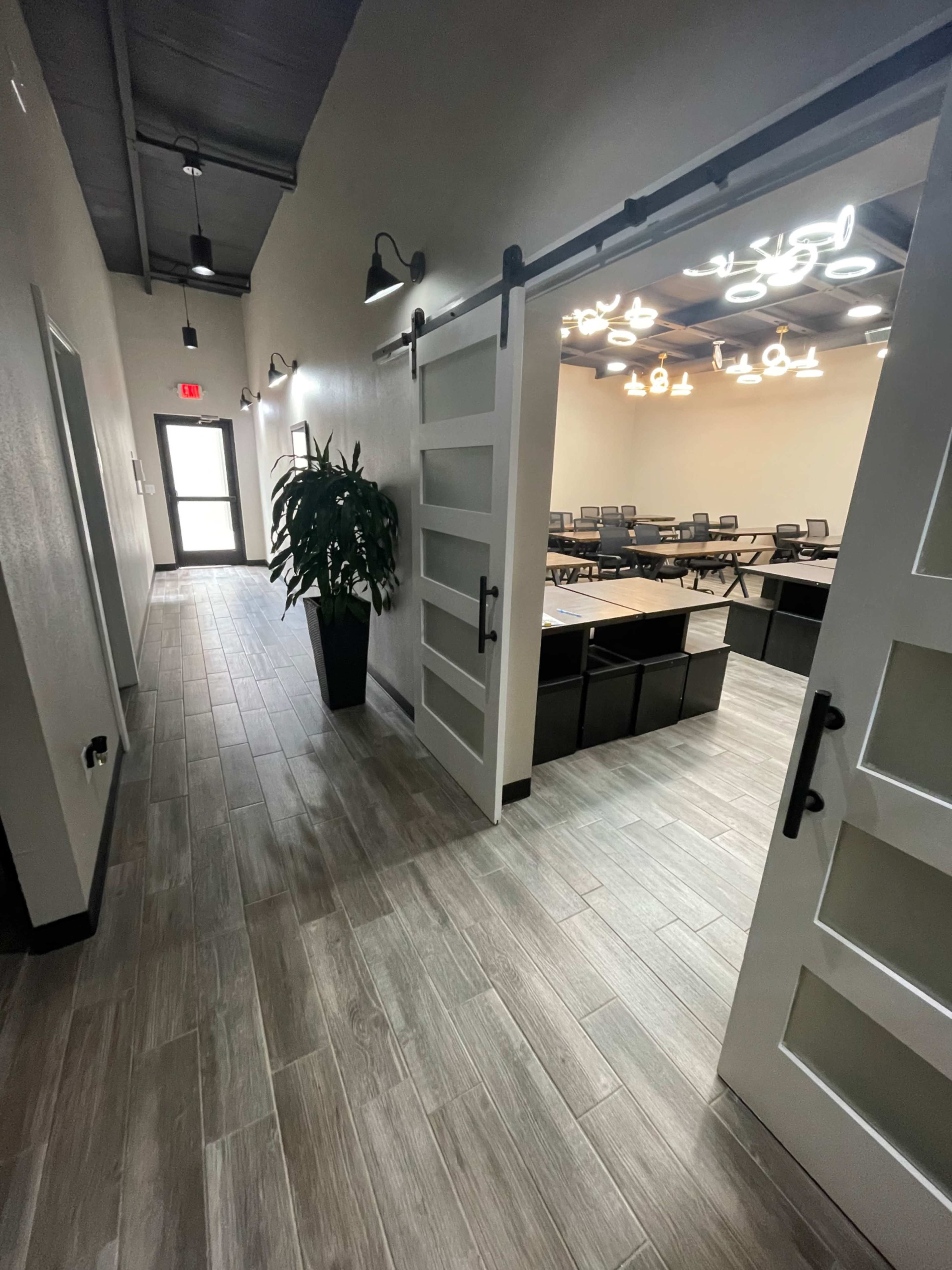 A well-lit hallway leads to a meeting room with a large table and chairs, framed by sliding doors and a potted plant nearby.