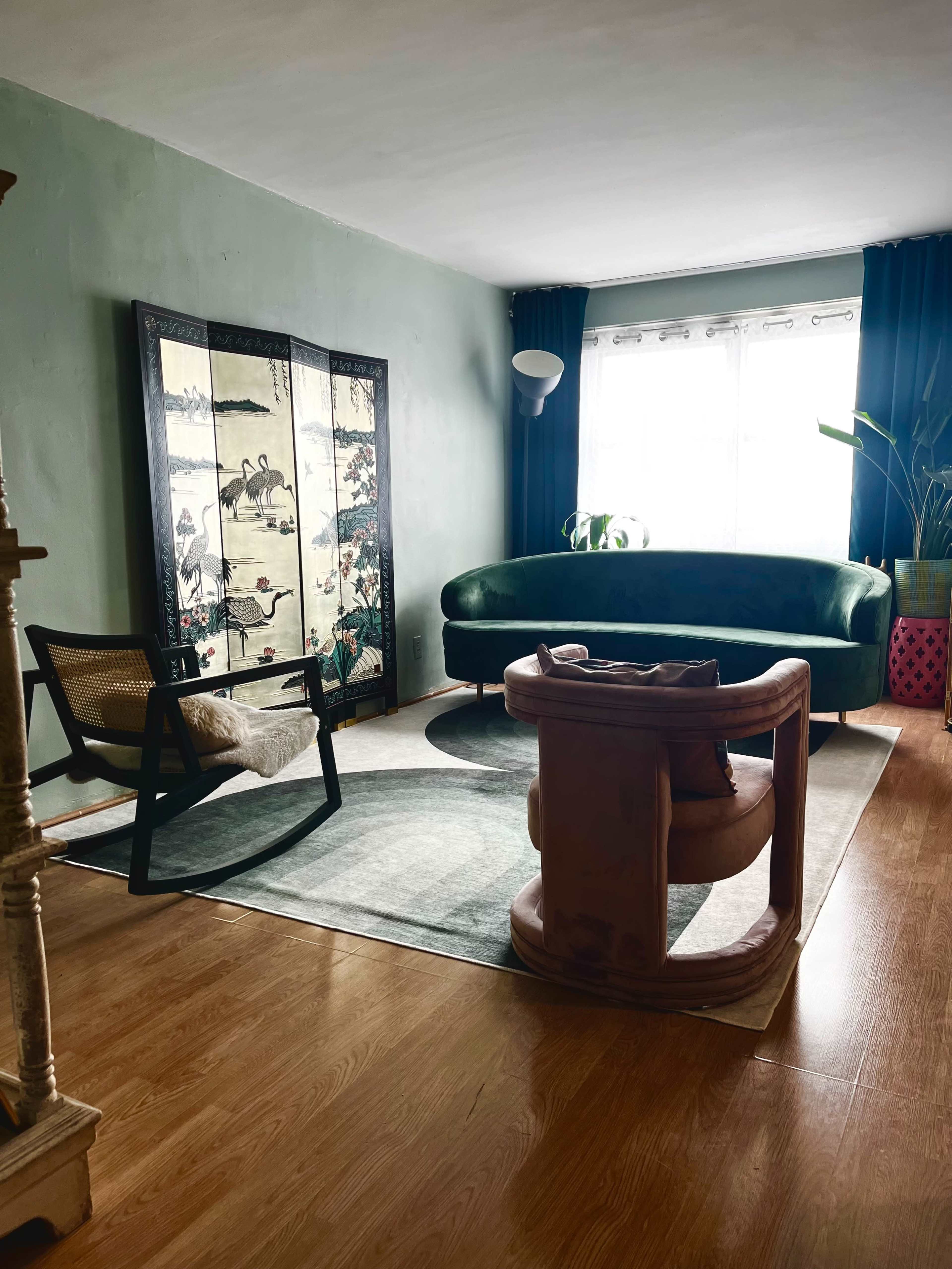 The living room features a green curved sofa, an accent chair, a decorative screen, and large windows with curtains.