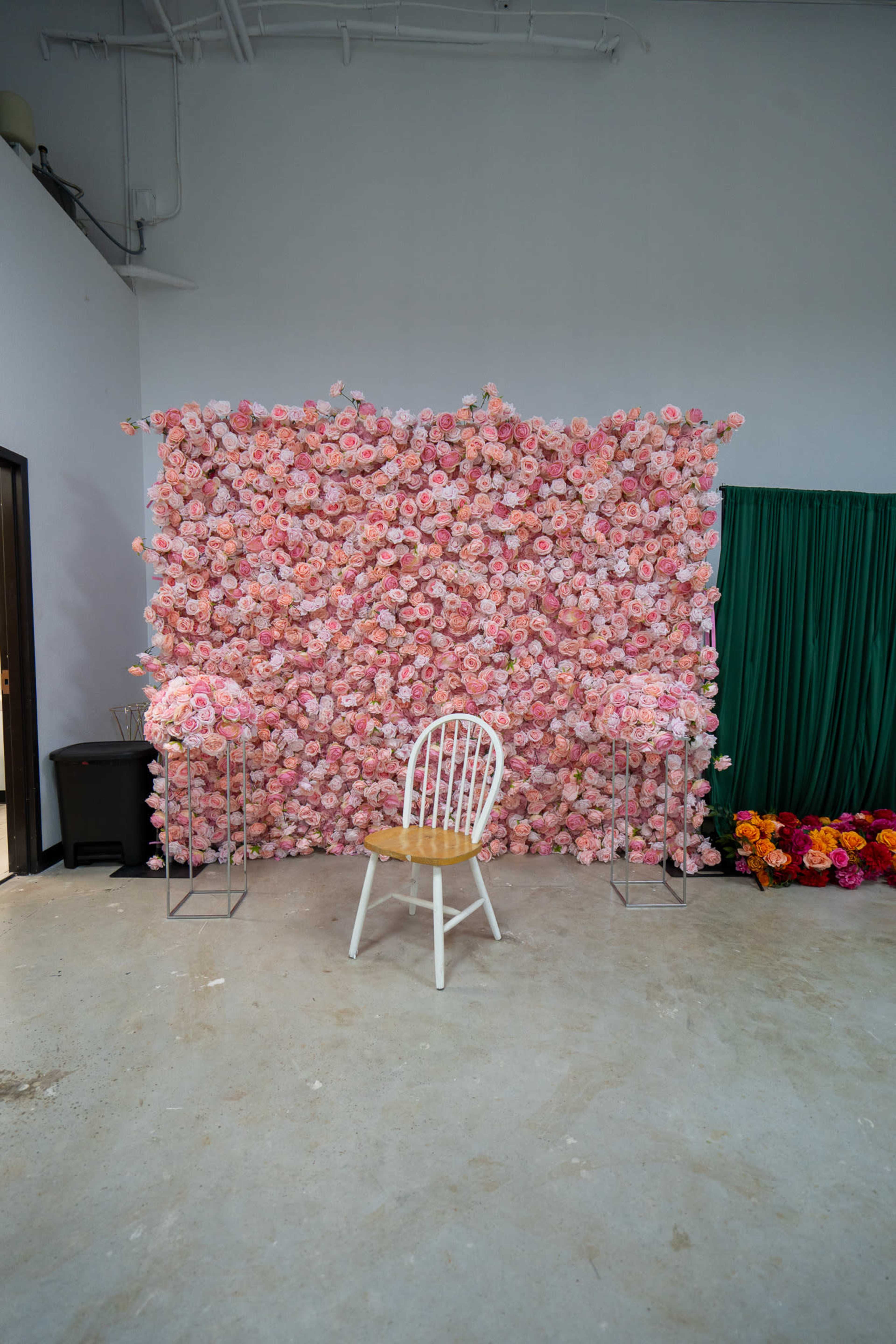 A white chair is positioned in front of a wall covered with a dense arrangement of pink flowers.
