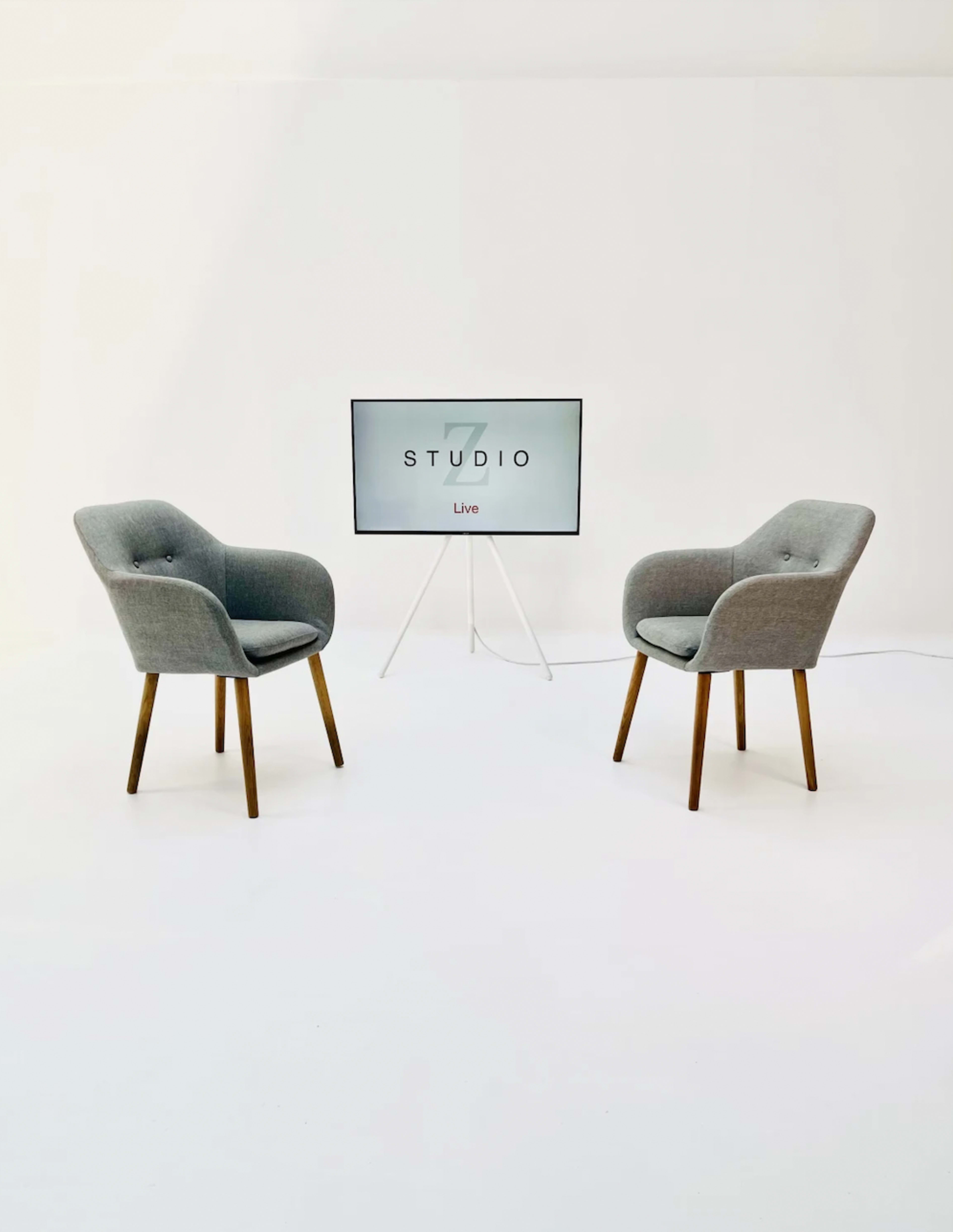 Two grey chairs are positioned opposite each other in front of a mounted screen displaying the word "STUDIO Live" on a plain white background.