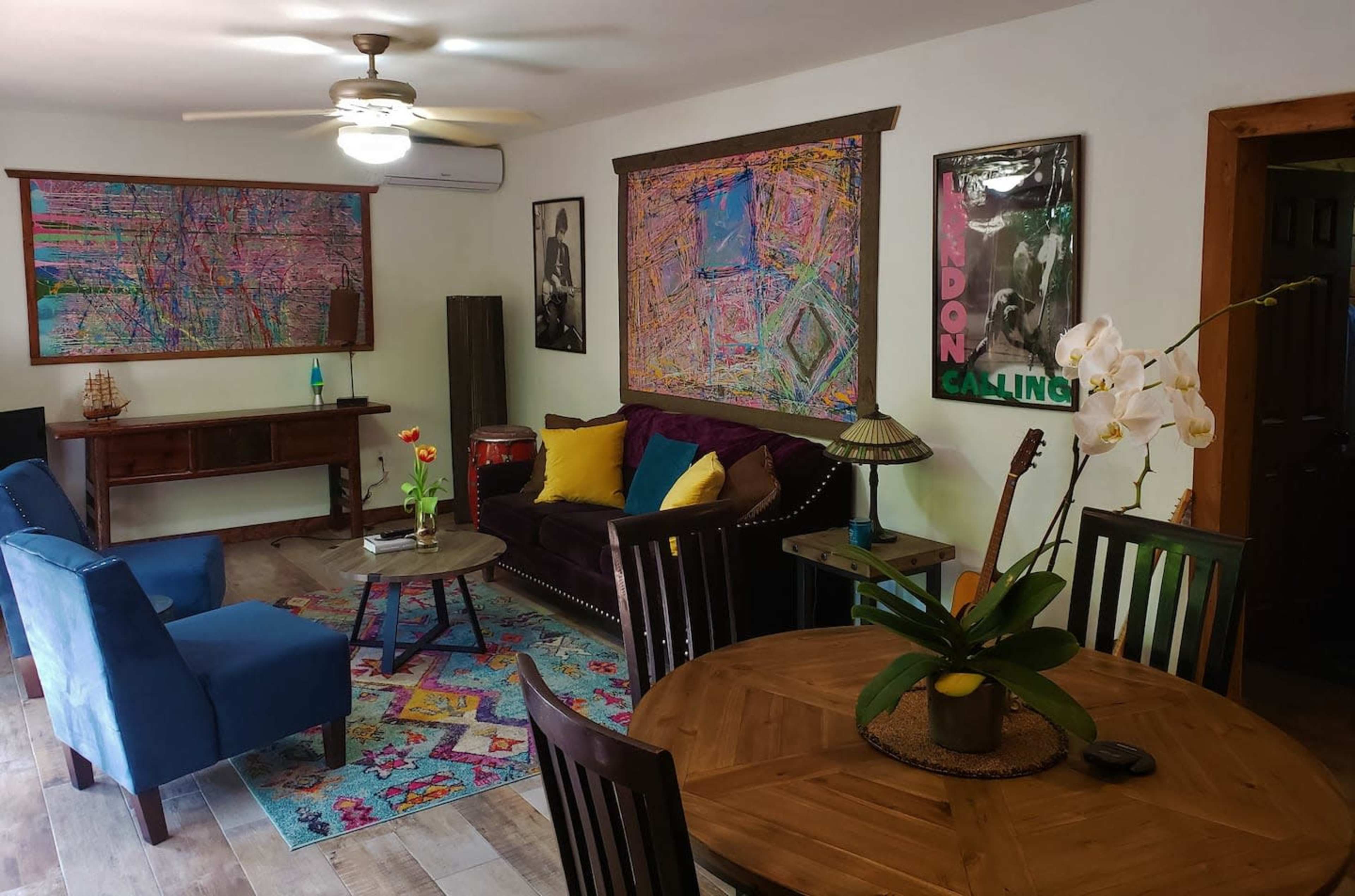 The room features a seating area with a purple couch, blue chairs, a wooden table, and colorful abstract artwork on the walls.