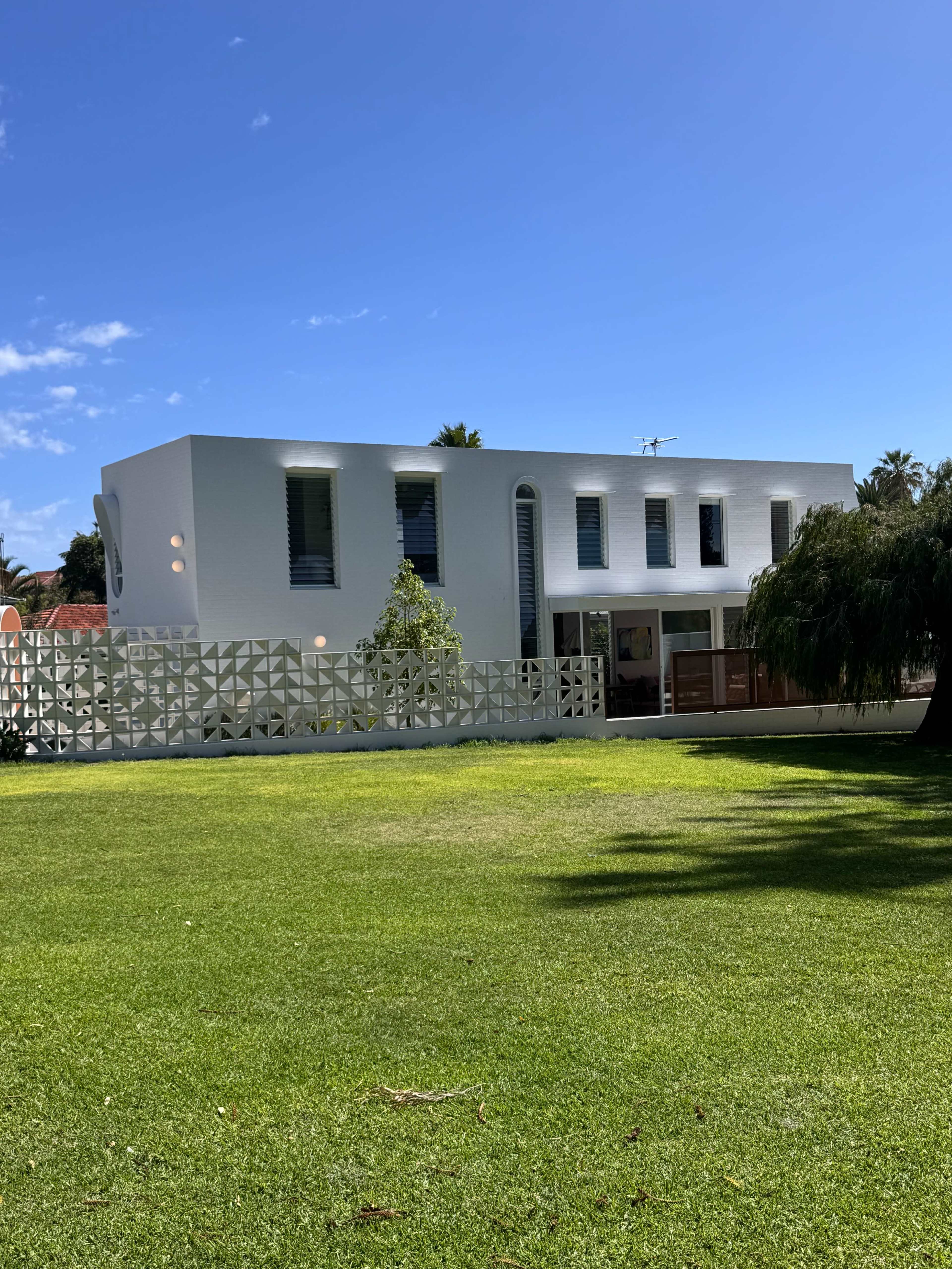 A modern white building with geometric patterns on its exterior is situated on a grassy lawn under a clear blue sky.