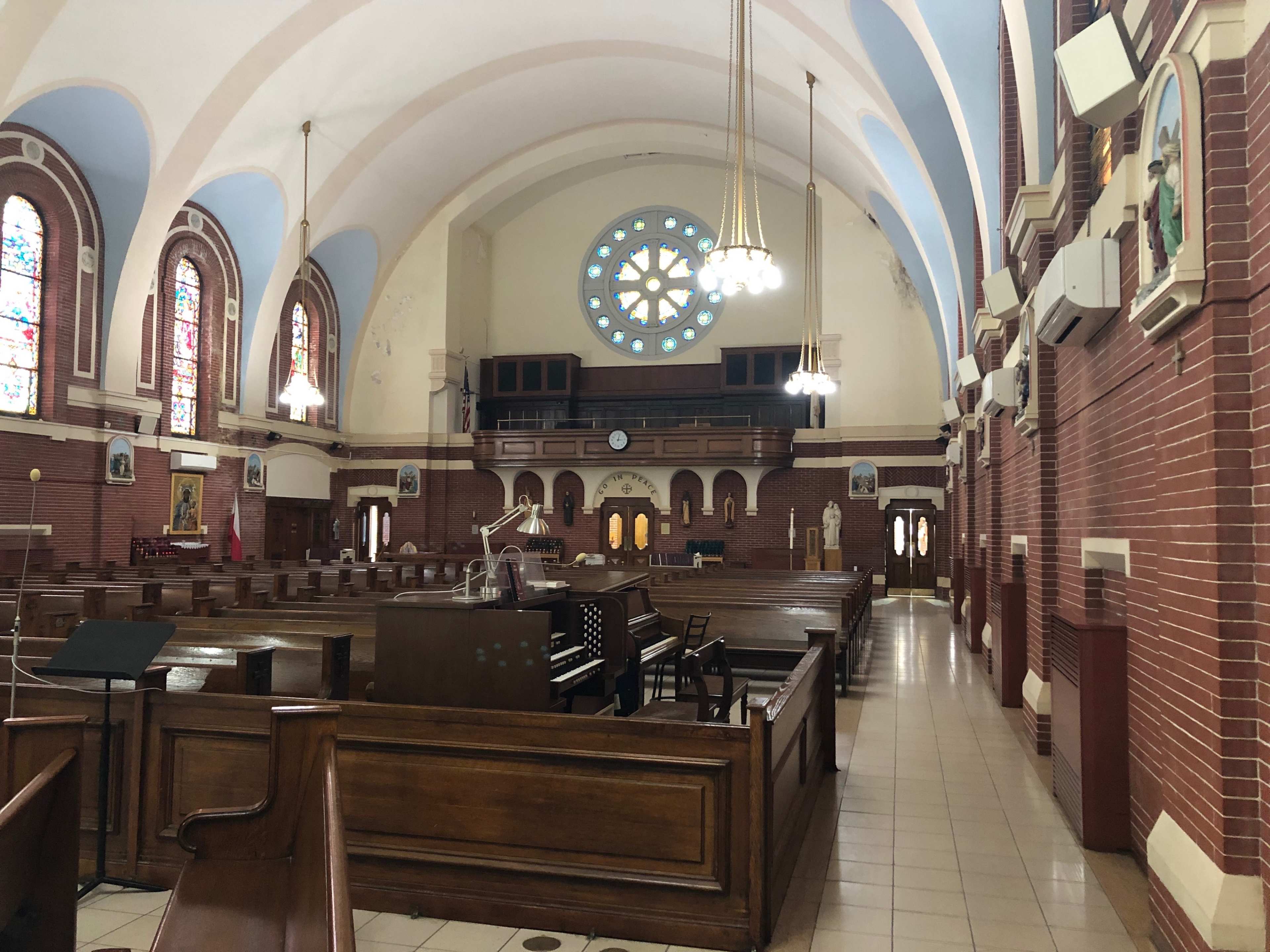 The interior of a church features wooden pews, a large stained glass window, and ornate chandeliers hanging from a high ceiling.