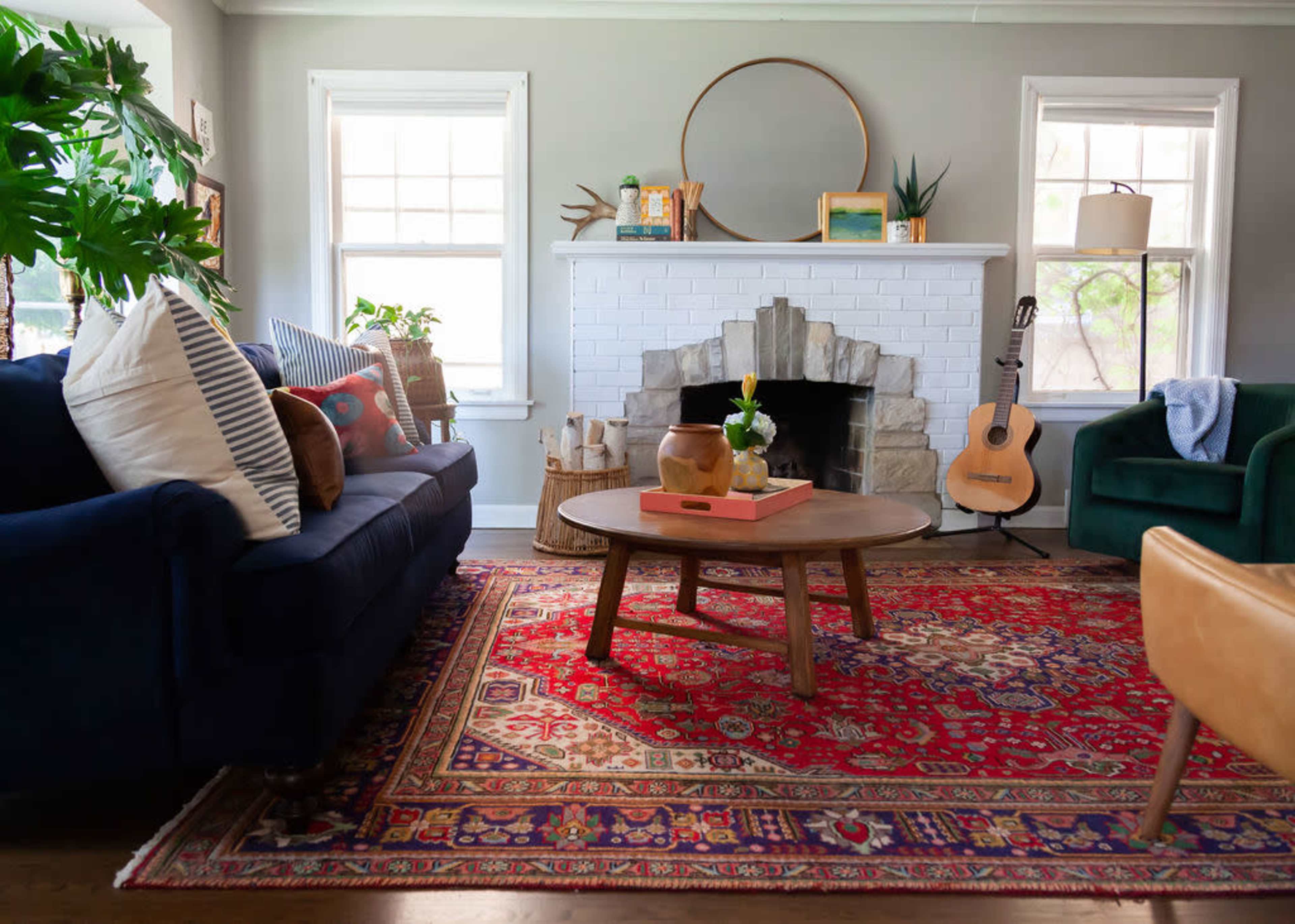 The living room features a blue sofa, a round wooden coffee table, a stone fireplace, and natural light streaming in through the windows.