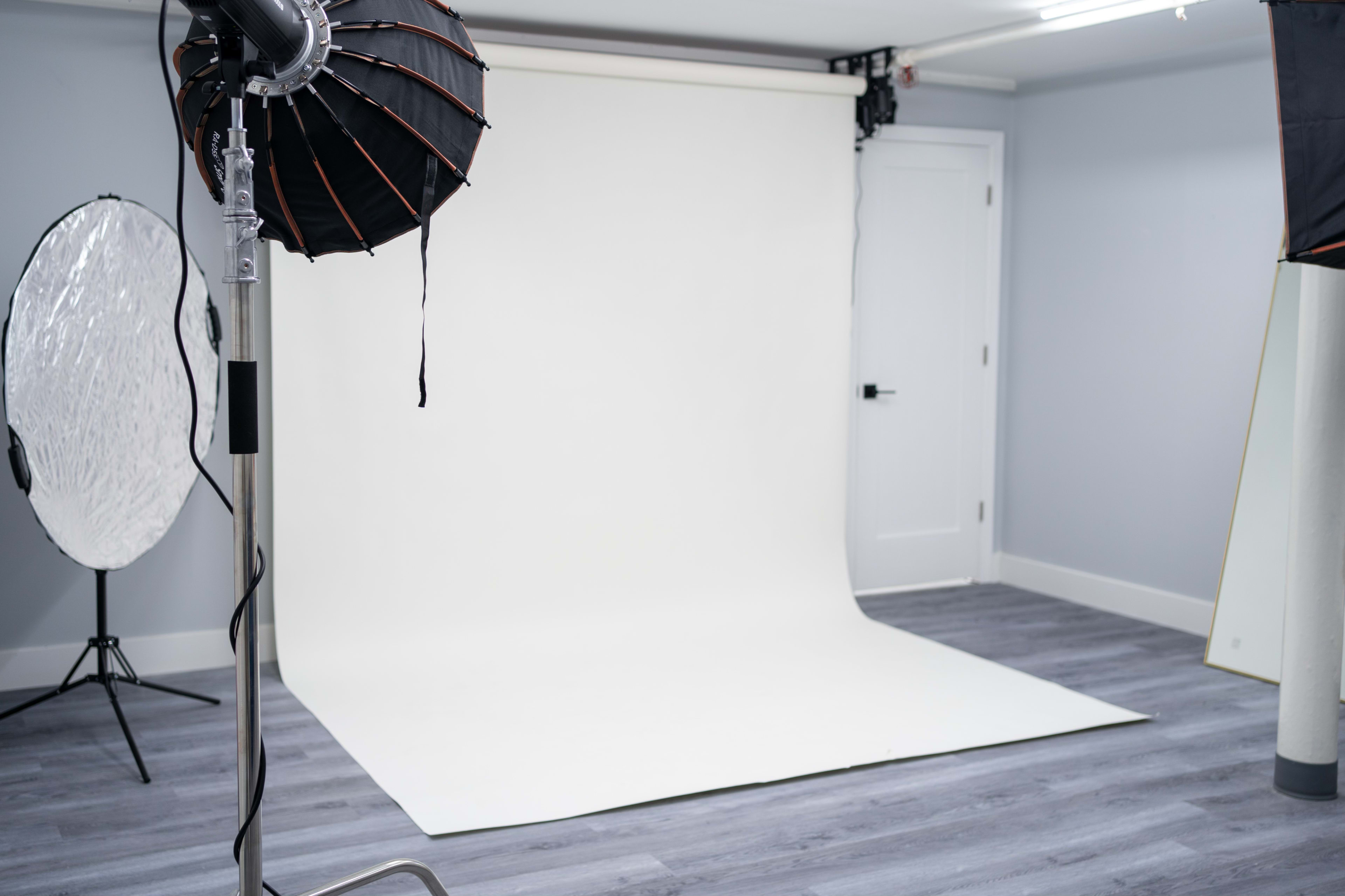 A photography studio with a white backdrop, lighting equipment, and a round reflector.