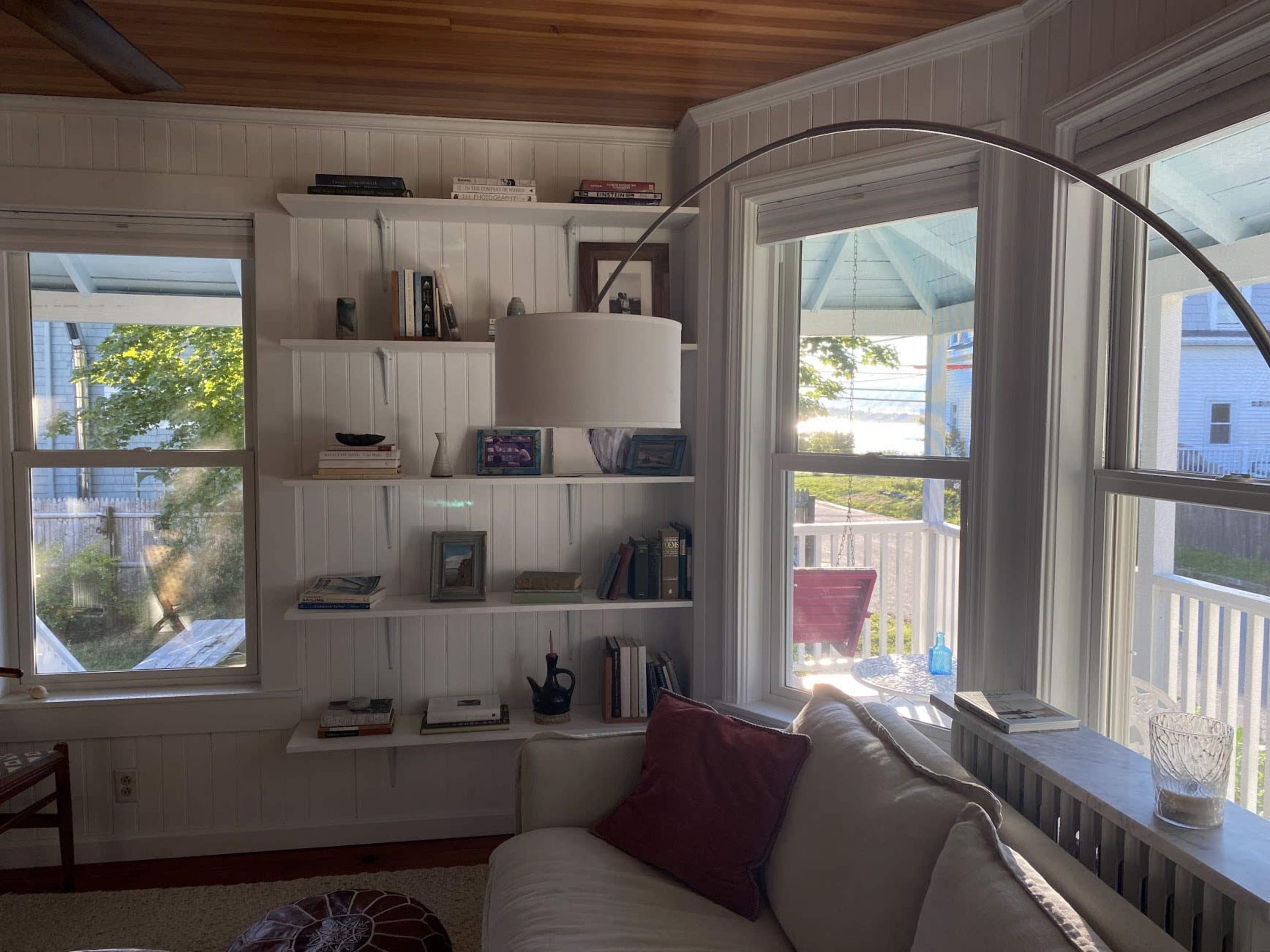 A bright living room with a white sofa, bookshelves filled with books and decor, and large windows overlooking a patio.