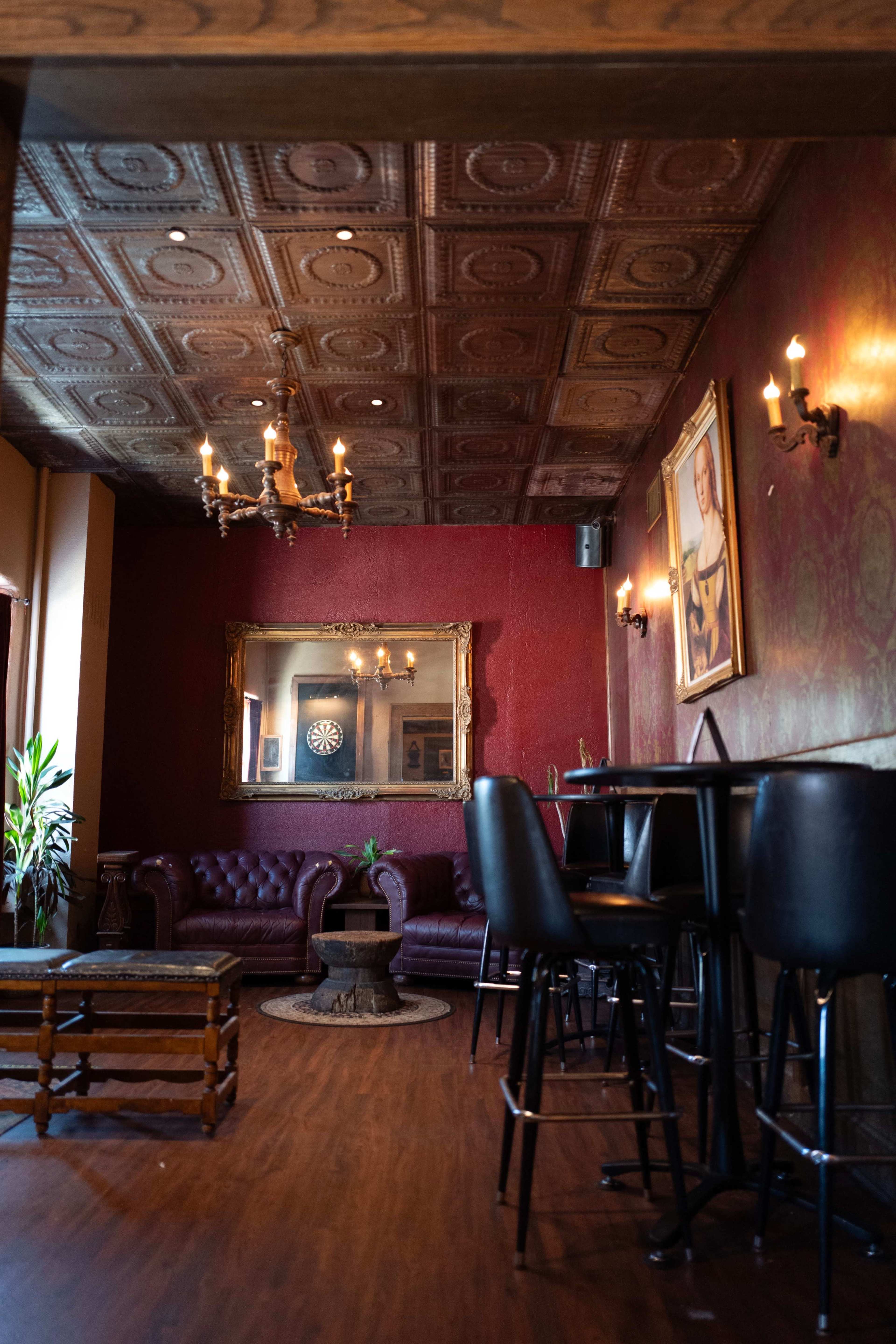 The interior of a dimly lit lounge features a red wall, vintage decor, a leather sofa, and a small dartboard in the background.