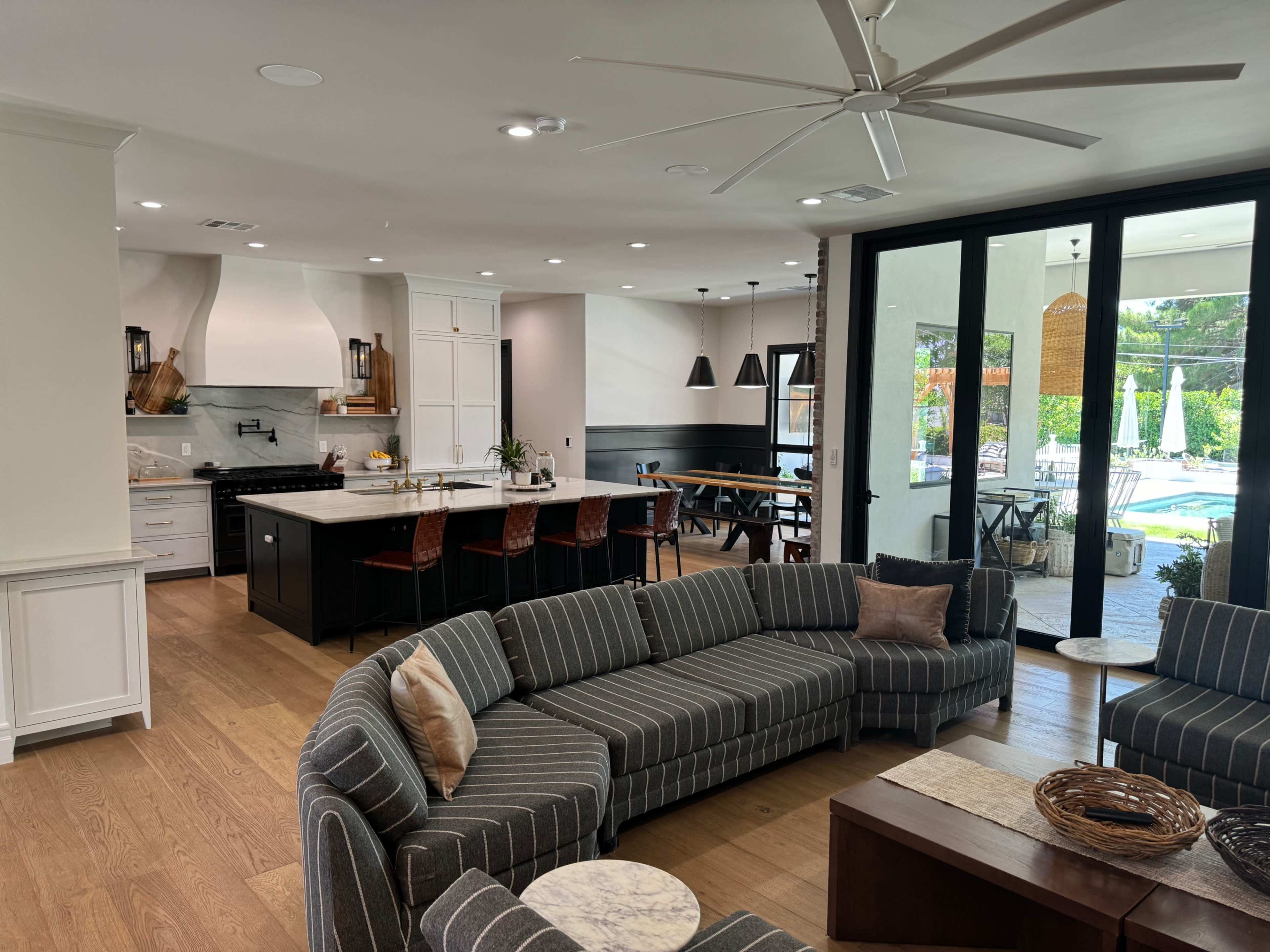 An open-concept living area featuring a striped sectional sofa, a modern kitchen with a large island, and large glass doors that open to a pool area.