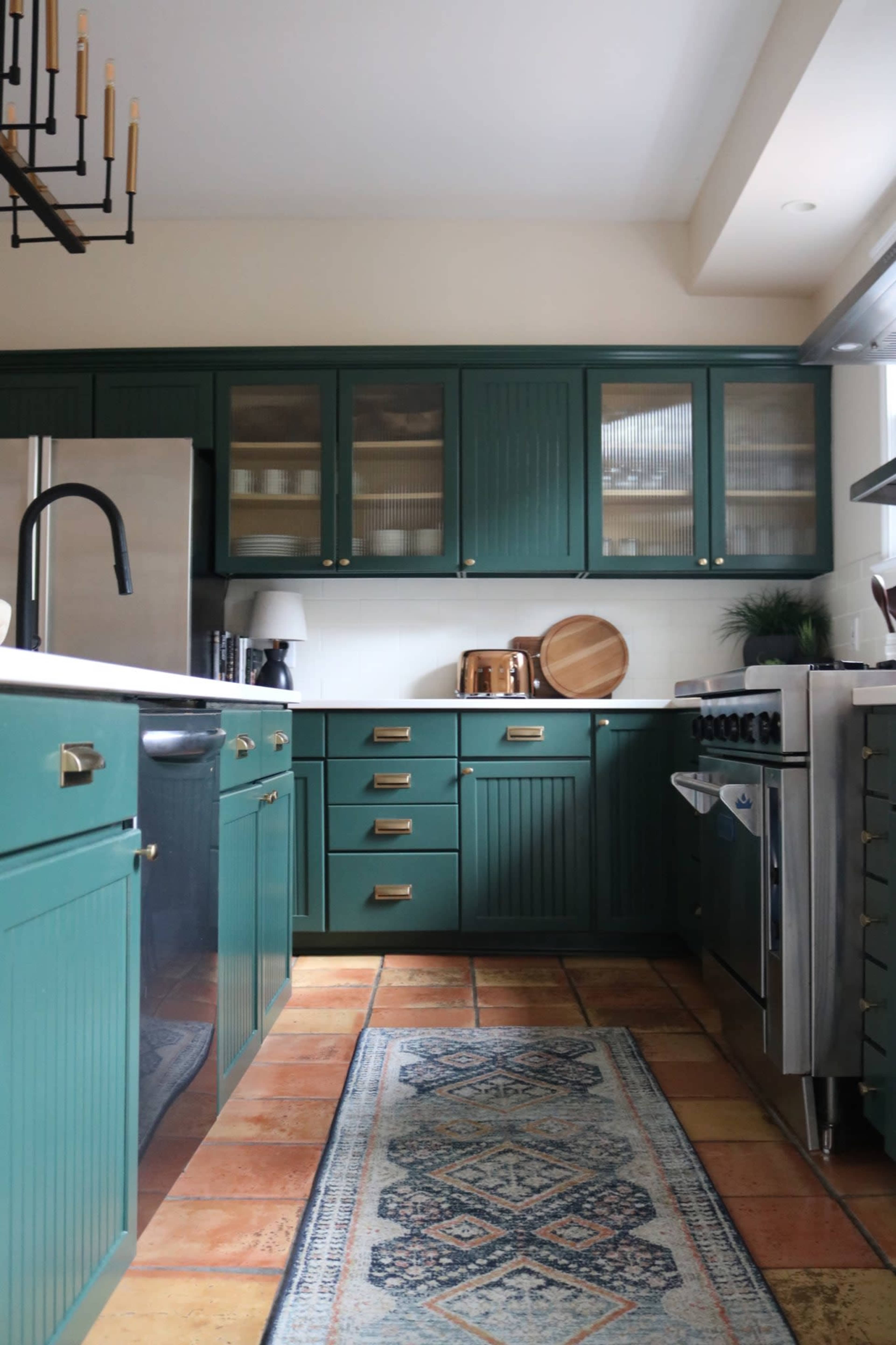 A green cabinet kitchen features stainless steel appliances, a decorative rug, and tile flooring.