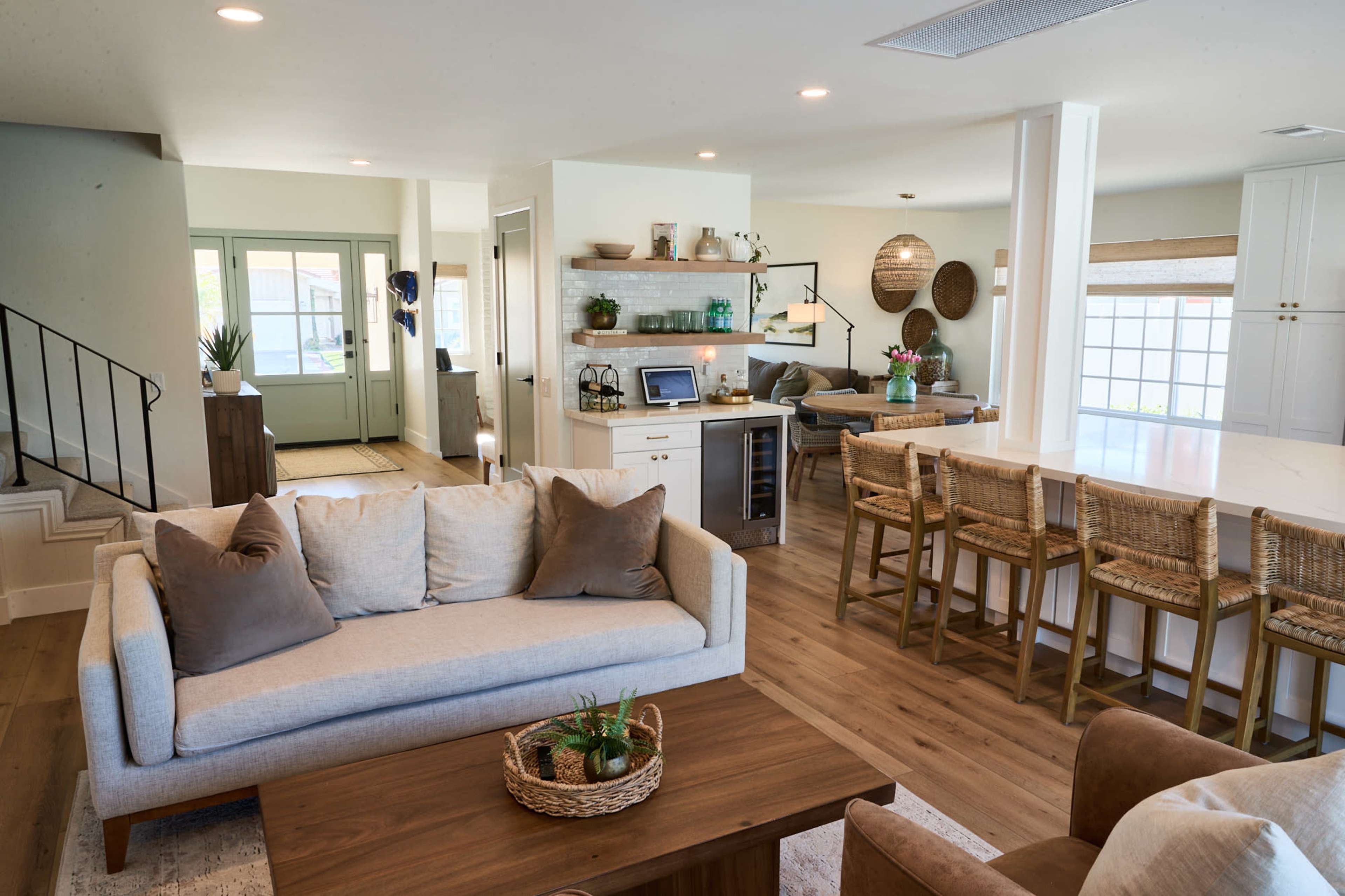 A modern open-concept living space featuring a beige couch, a wooden coffee table with a plant, and a kitchen area with bar seating.