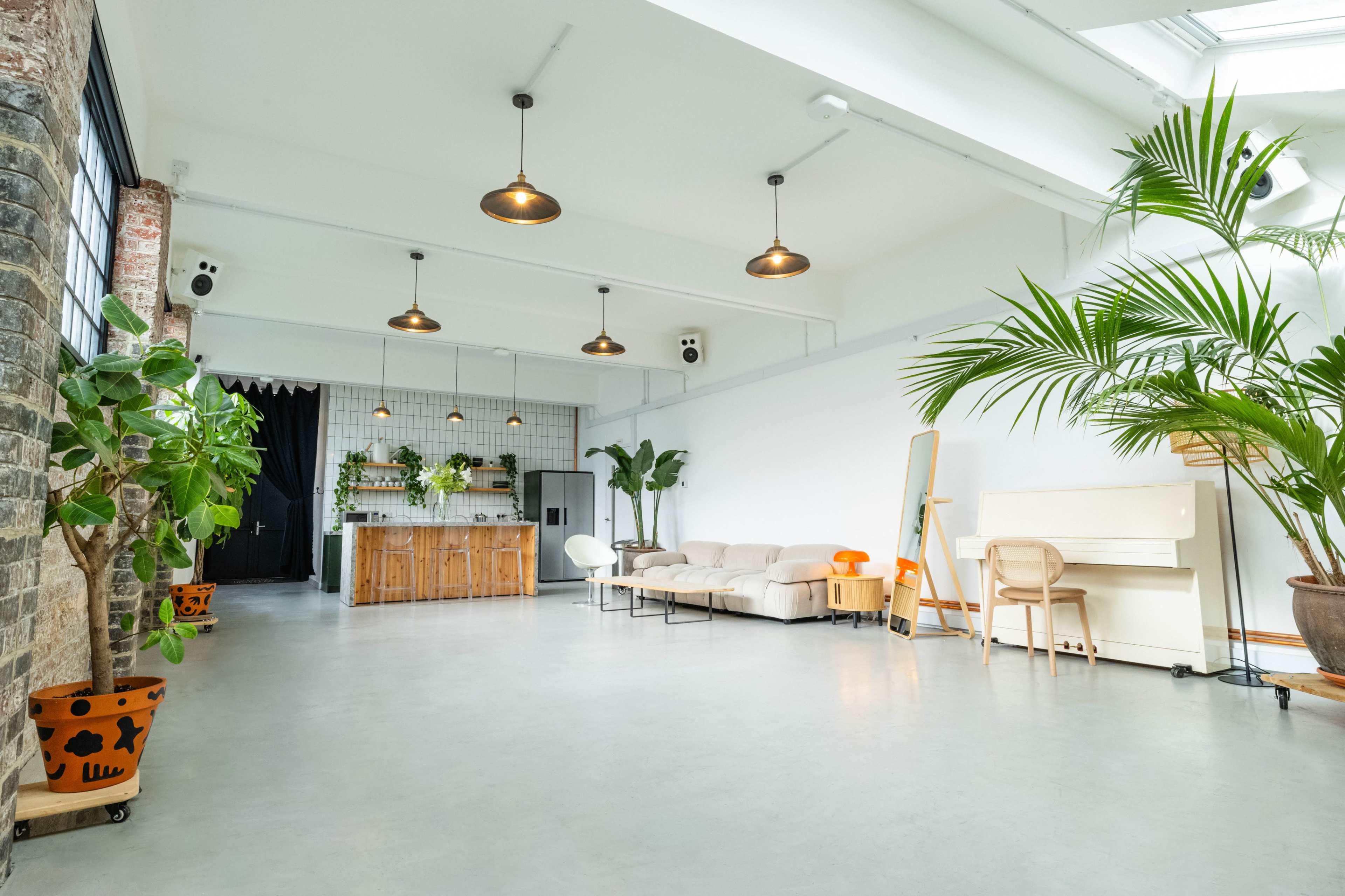 A spacious, modern interior with a kitchen area, a sofa, a piano, and several potted plants.
