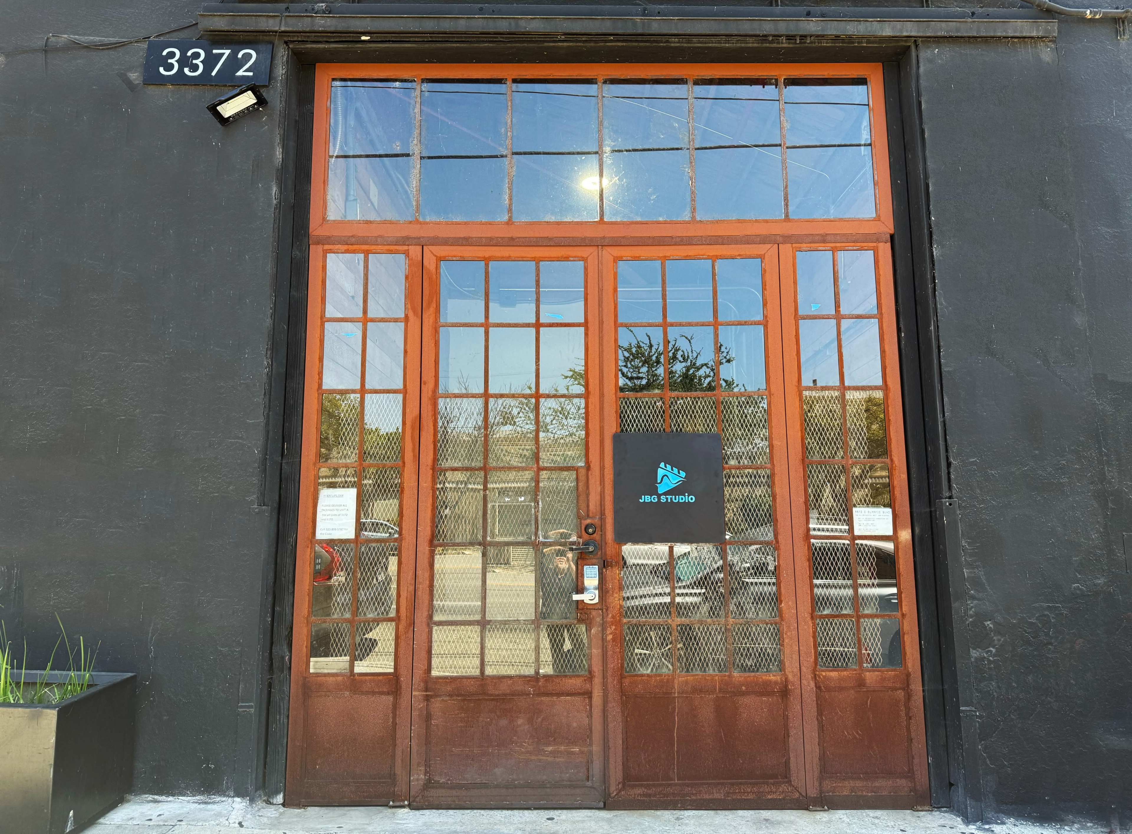 The image shows a large wooden double door with glass panels, marked with the number 3372, set against a black building facade.
