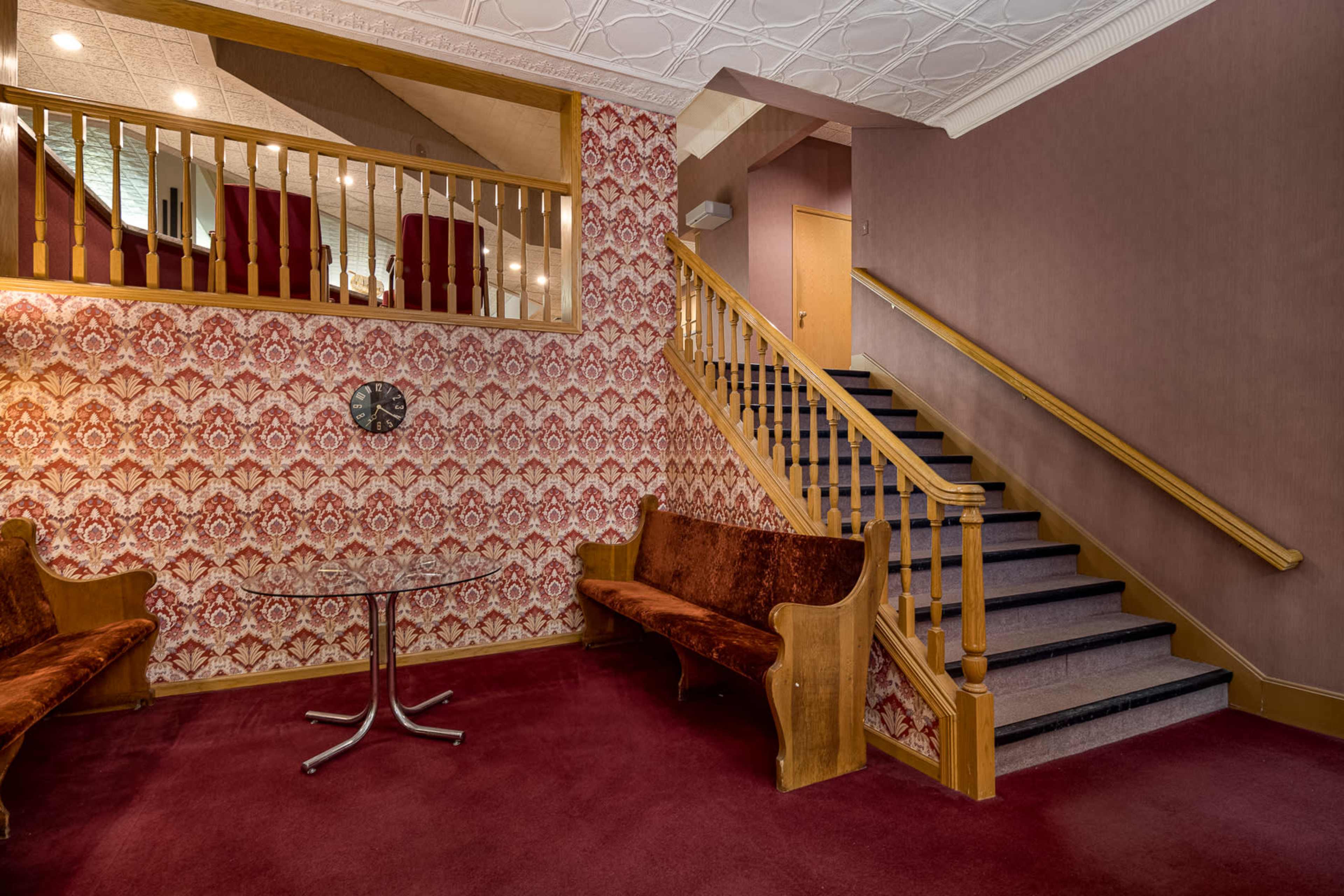 A foyer with patterned wallpaper, two brown upholstered benches, a round table, and a staircase leading to an upper level.