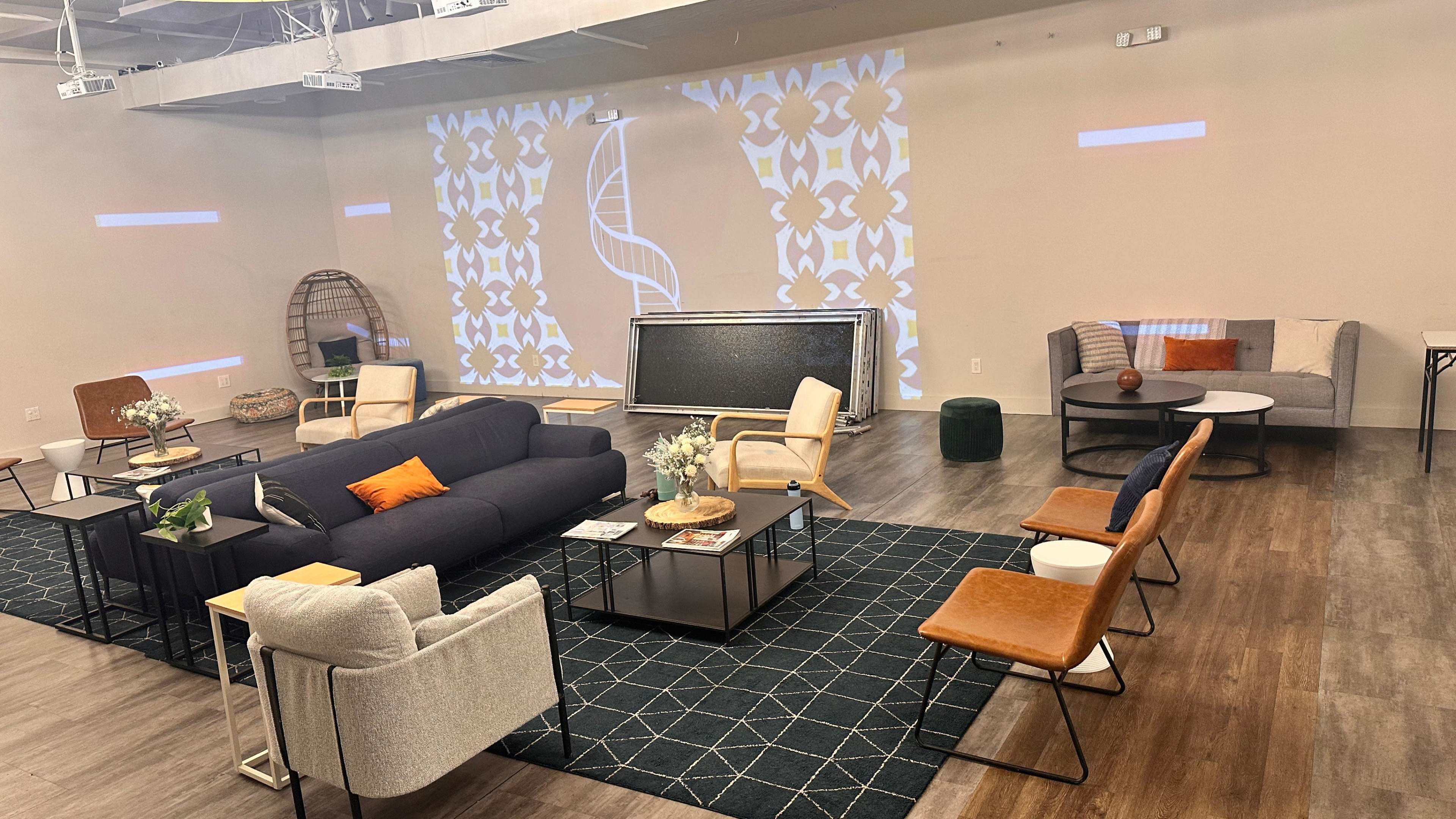 The image shows a modern, furnished lounge area with a mix of seating options, a large rug, and projected patterns on the walls.