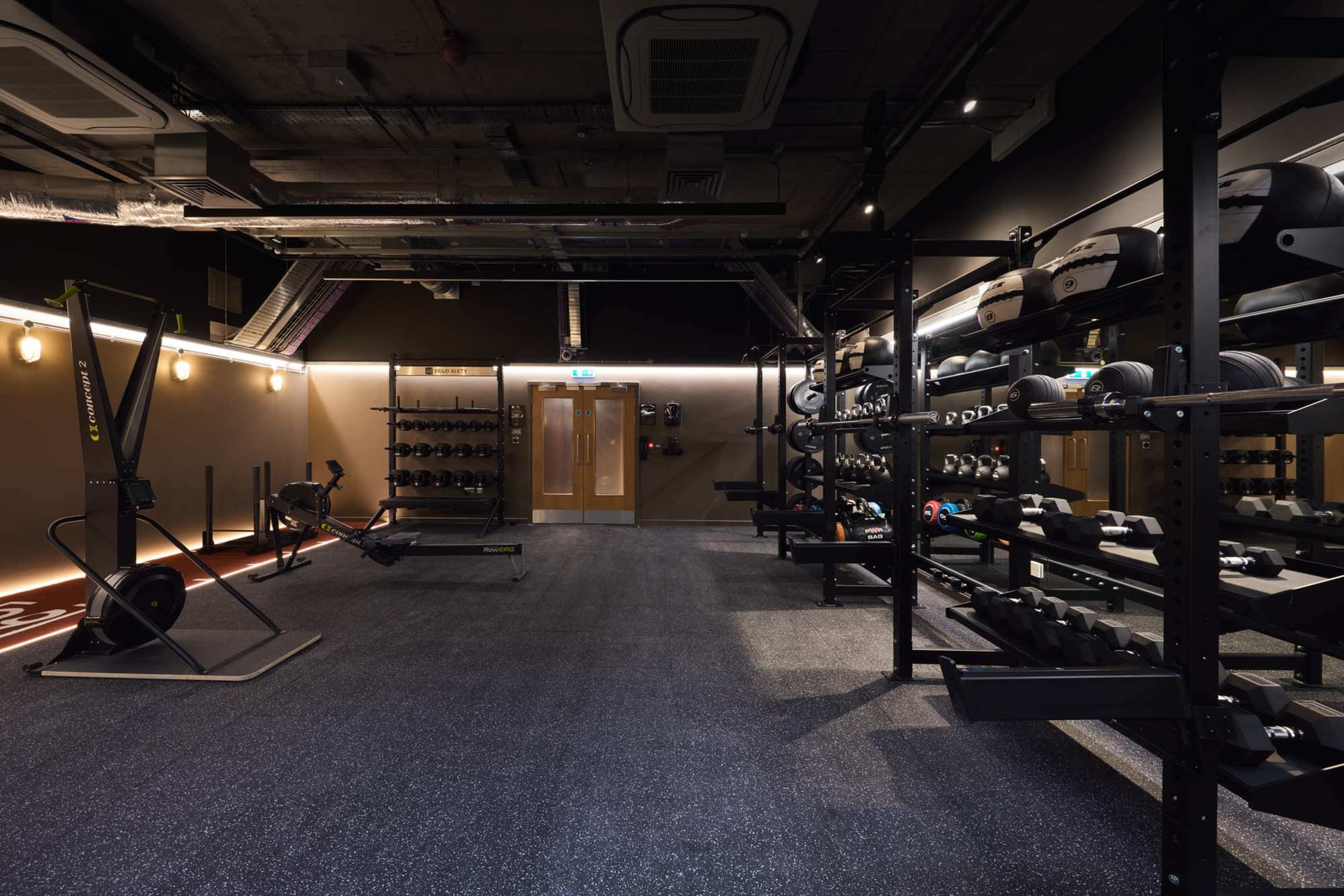 The image shows a well-equipped gym interior featuring various weights and exercise machines arranged neatly against the walls.