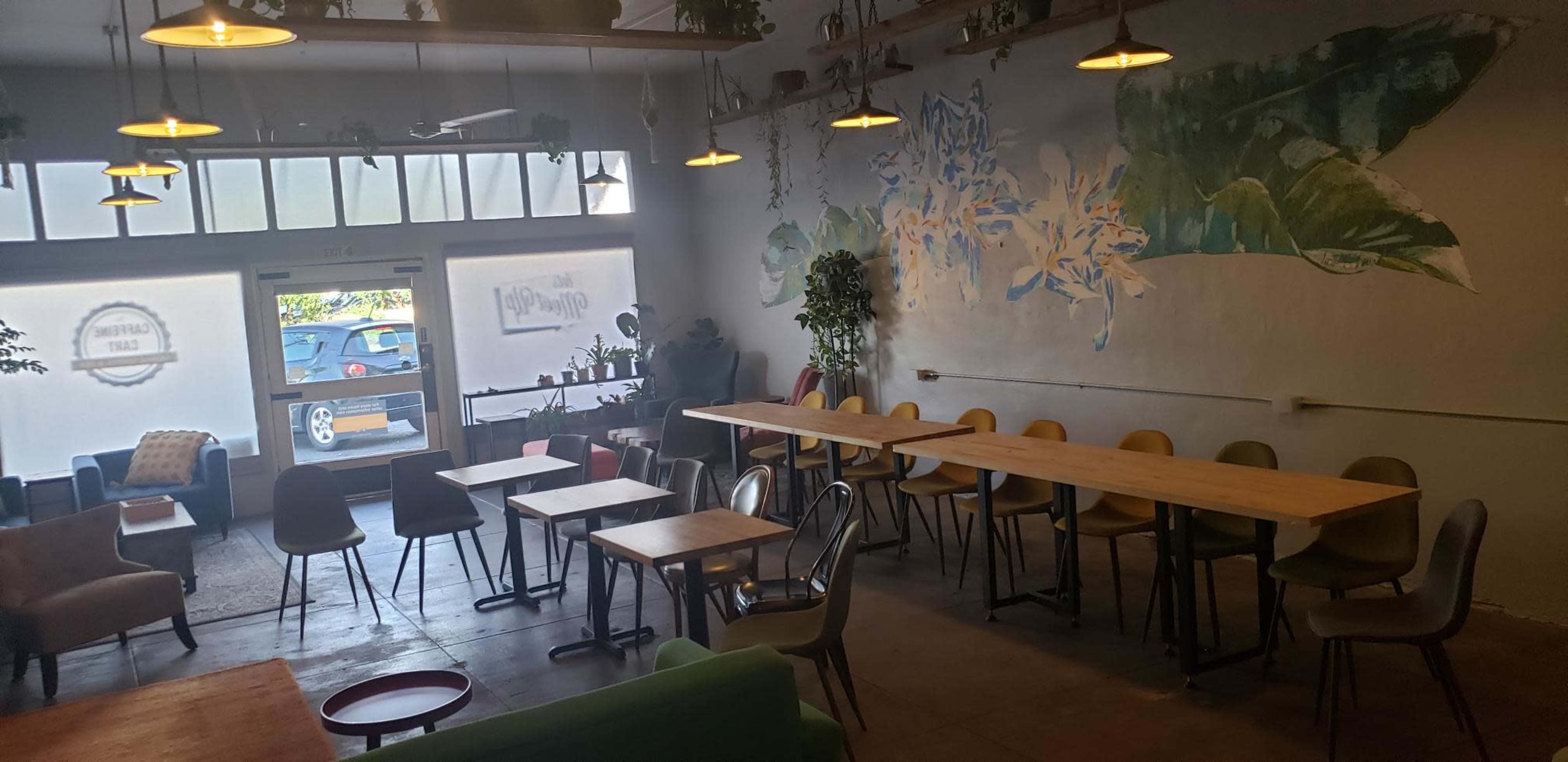 A cafe interior with various seating arrangements, including tables and chairs, against a wall adorned with a mural.