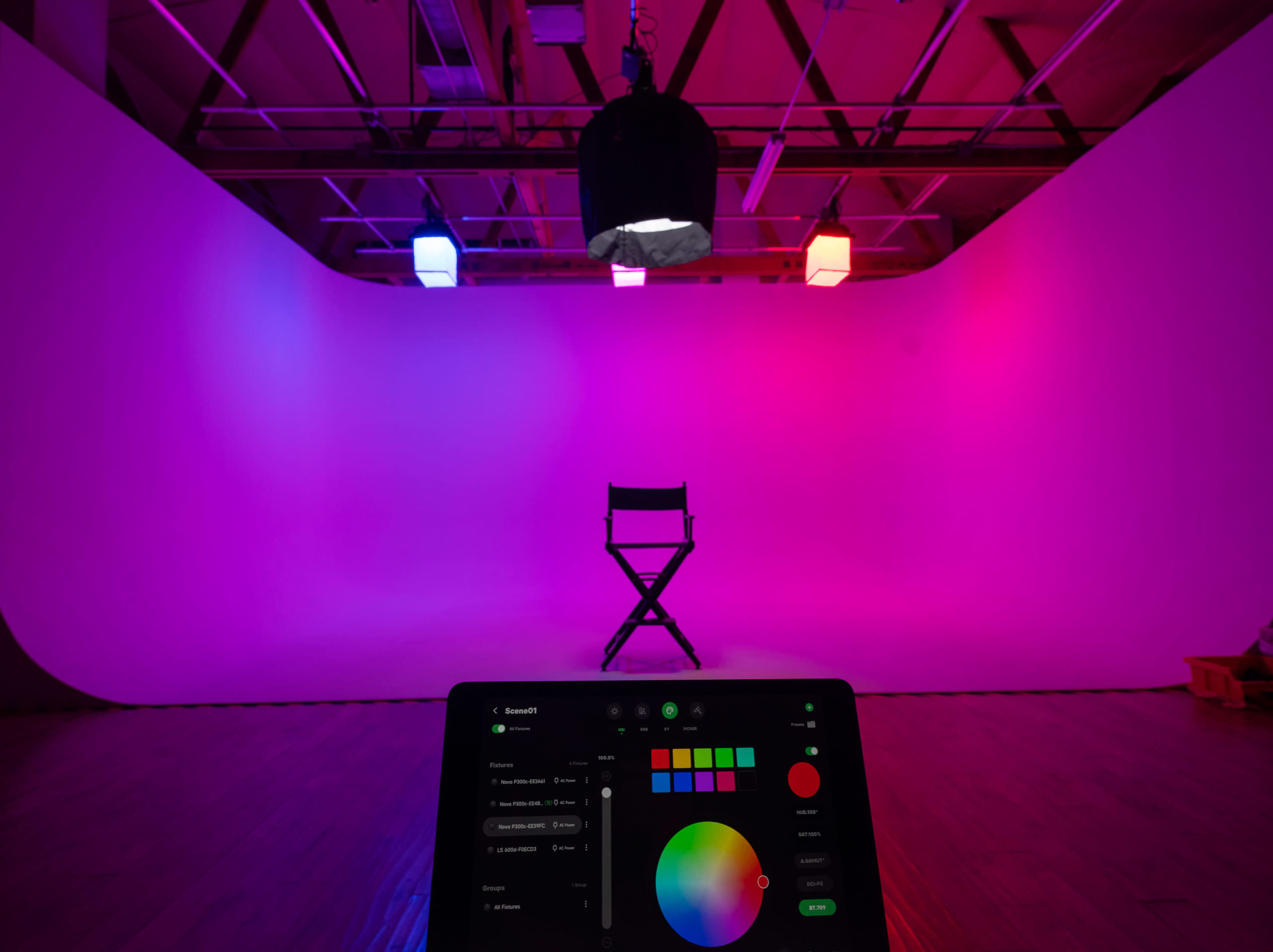 A photography studio features a single black director's chair in front of a lit, gradient backdrop with colored lights.
