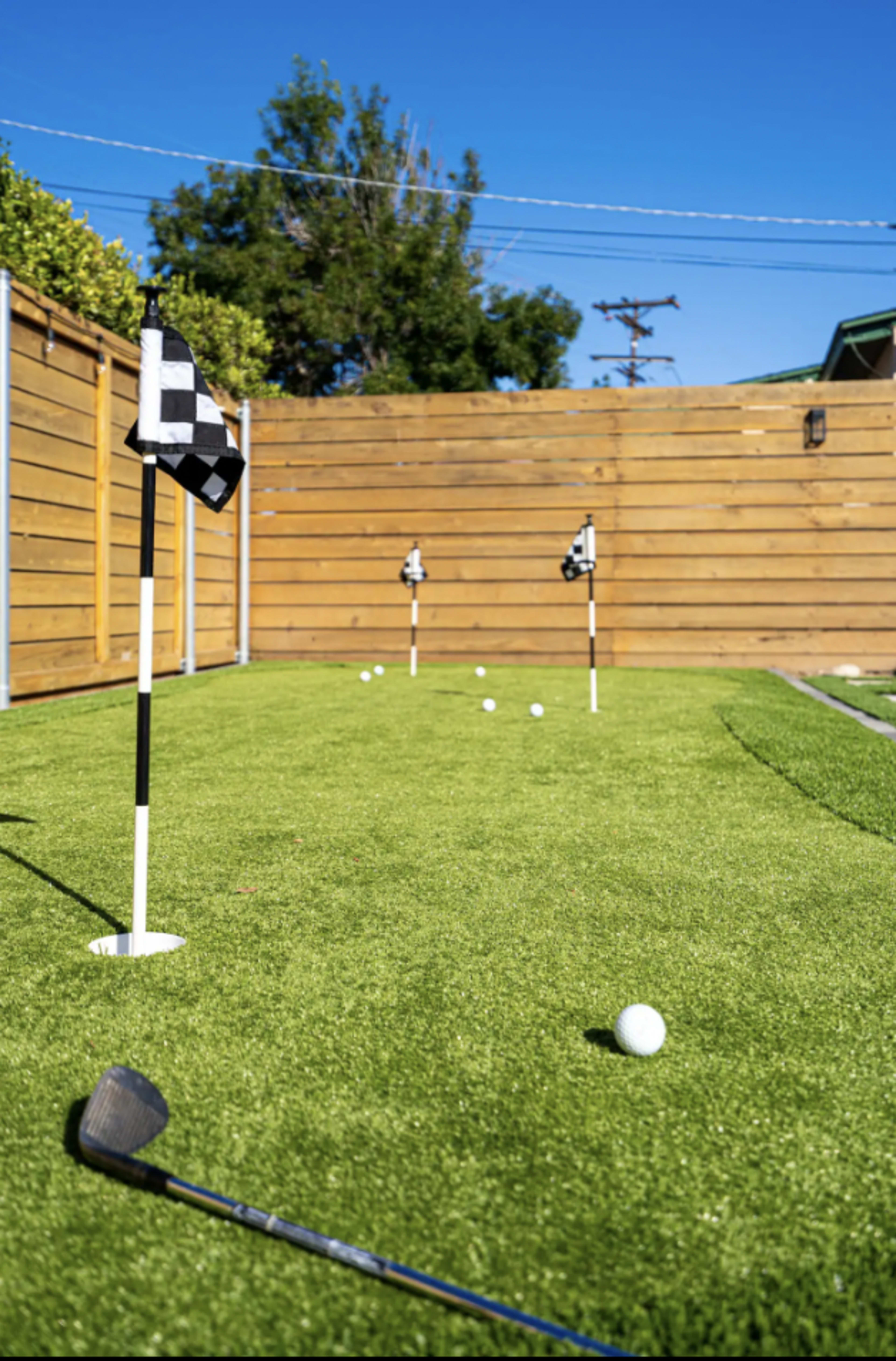 A putting green with several small flags and golf balls arranged in a backyard setting.