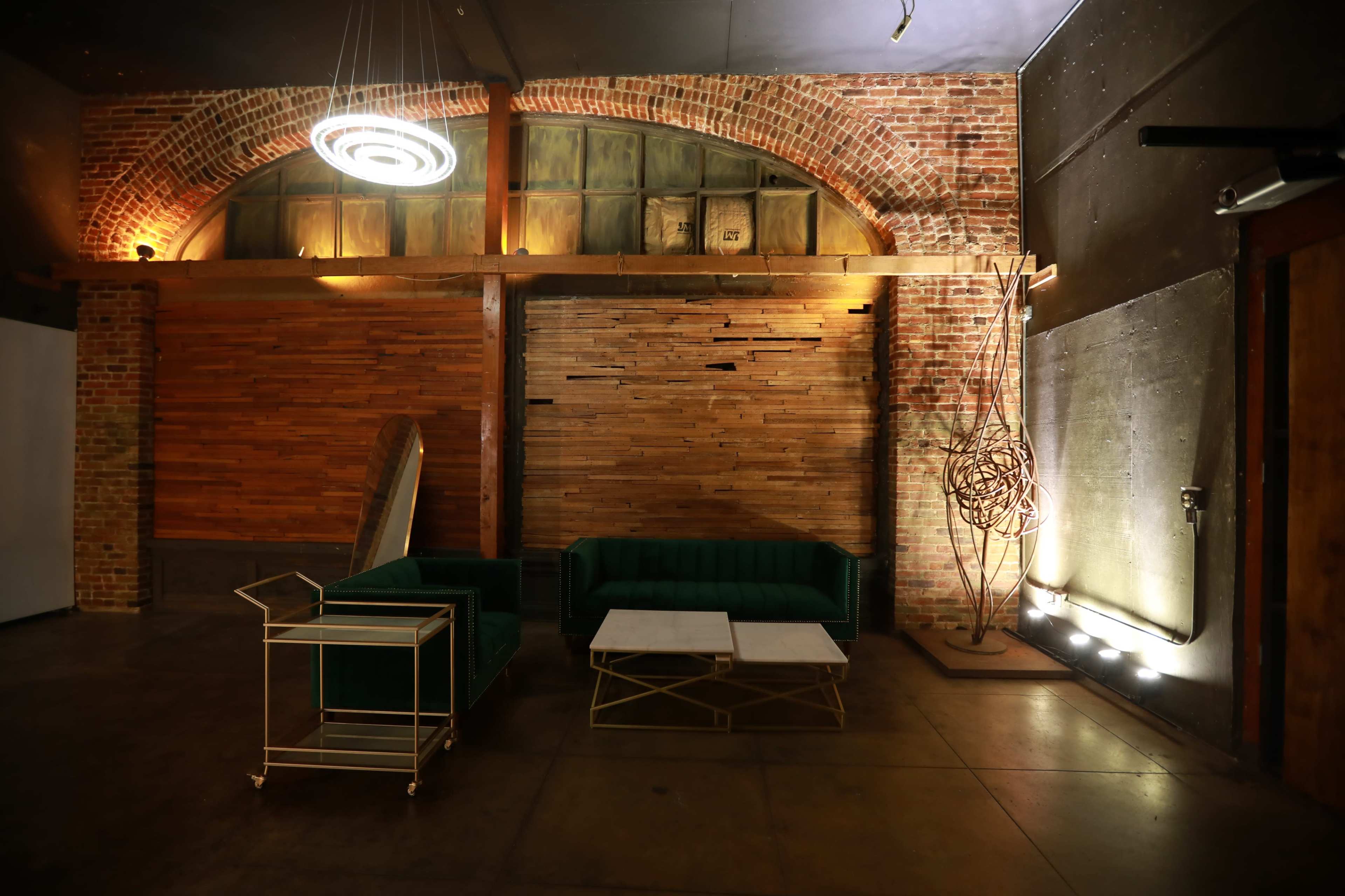 A modern interior space with a brick wall, wooden paneling, a green couch, two coffee tables, and ambient lighting.