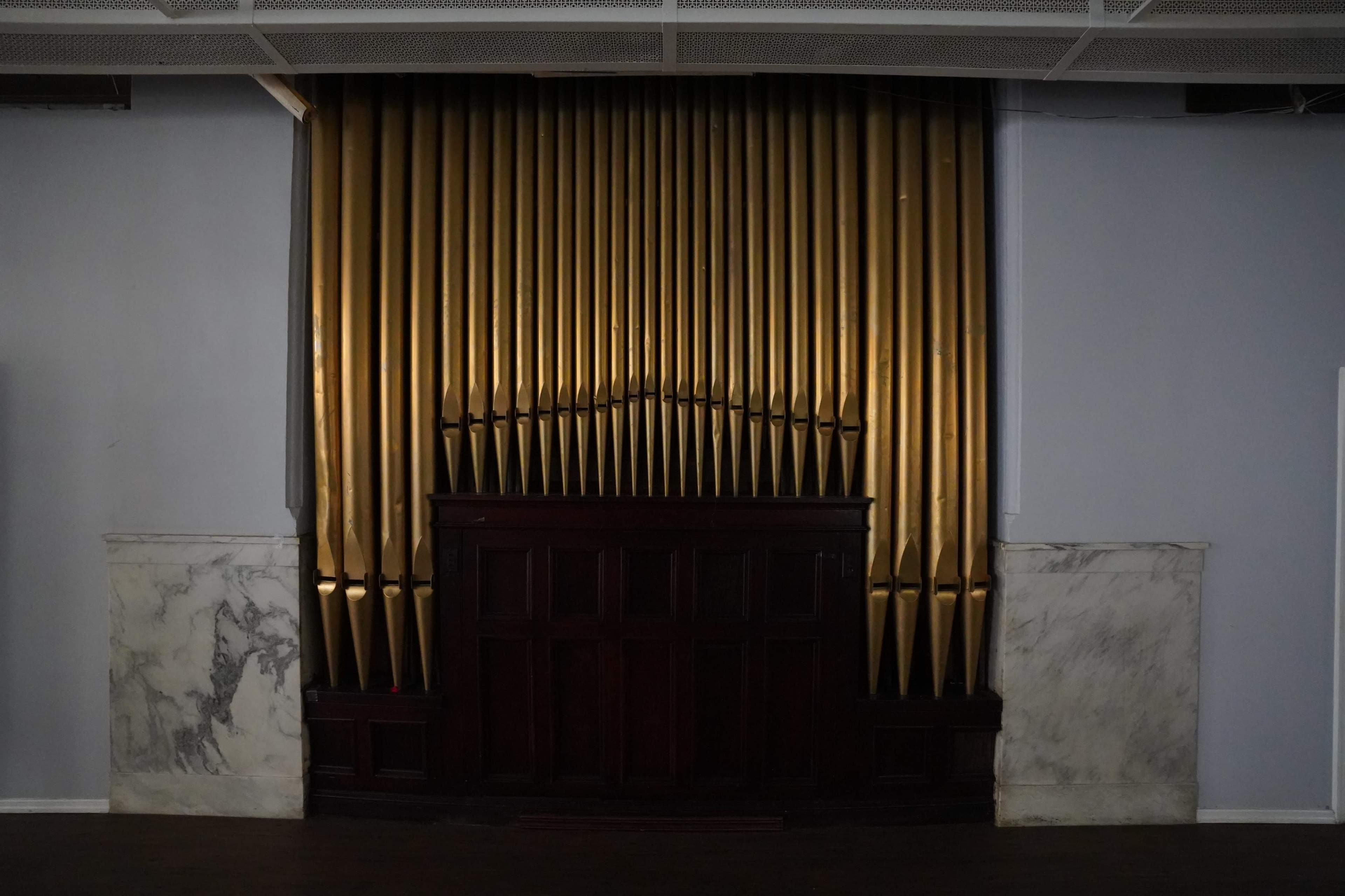 A wall with a set of golden organ pipes flanked by marble panels.
