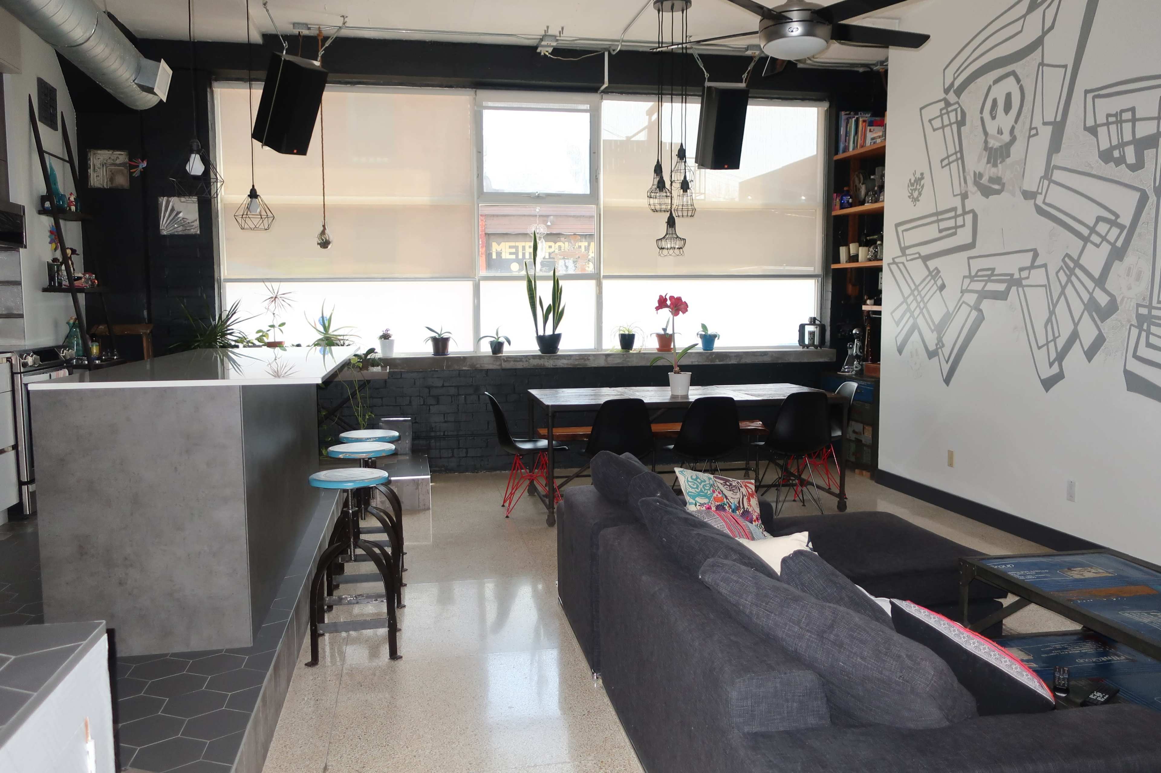 The image shows a modern open-concept living space with a kitchen area on the left and a dining area with a large table and chairs on the right, accented by a wall mural.