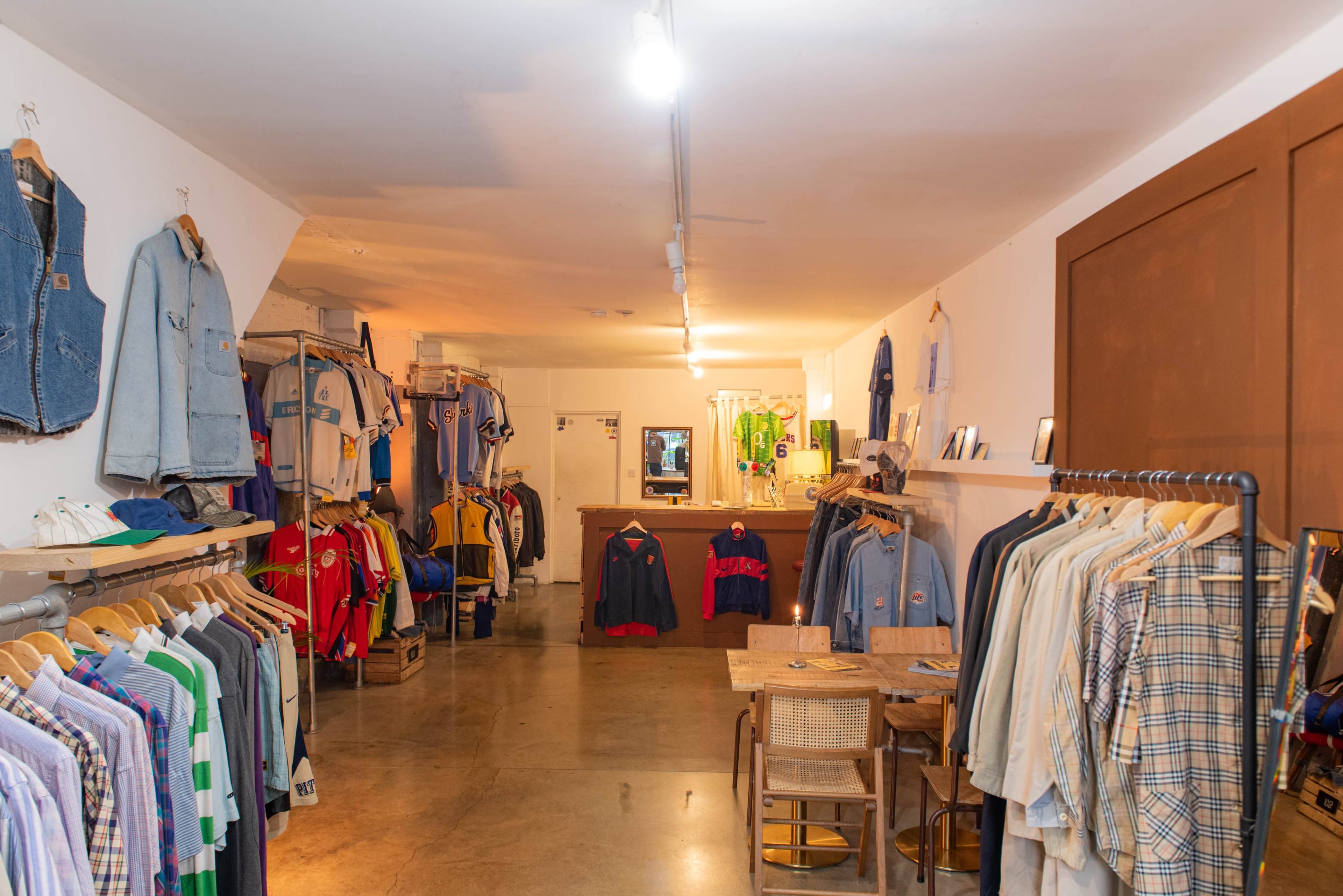 The image shows a clothing store interior with racks of various apparel, including shirts and jackets, arranged along the walls and a counter at the back.