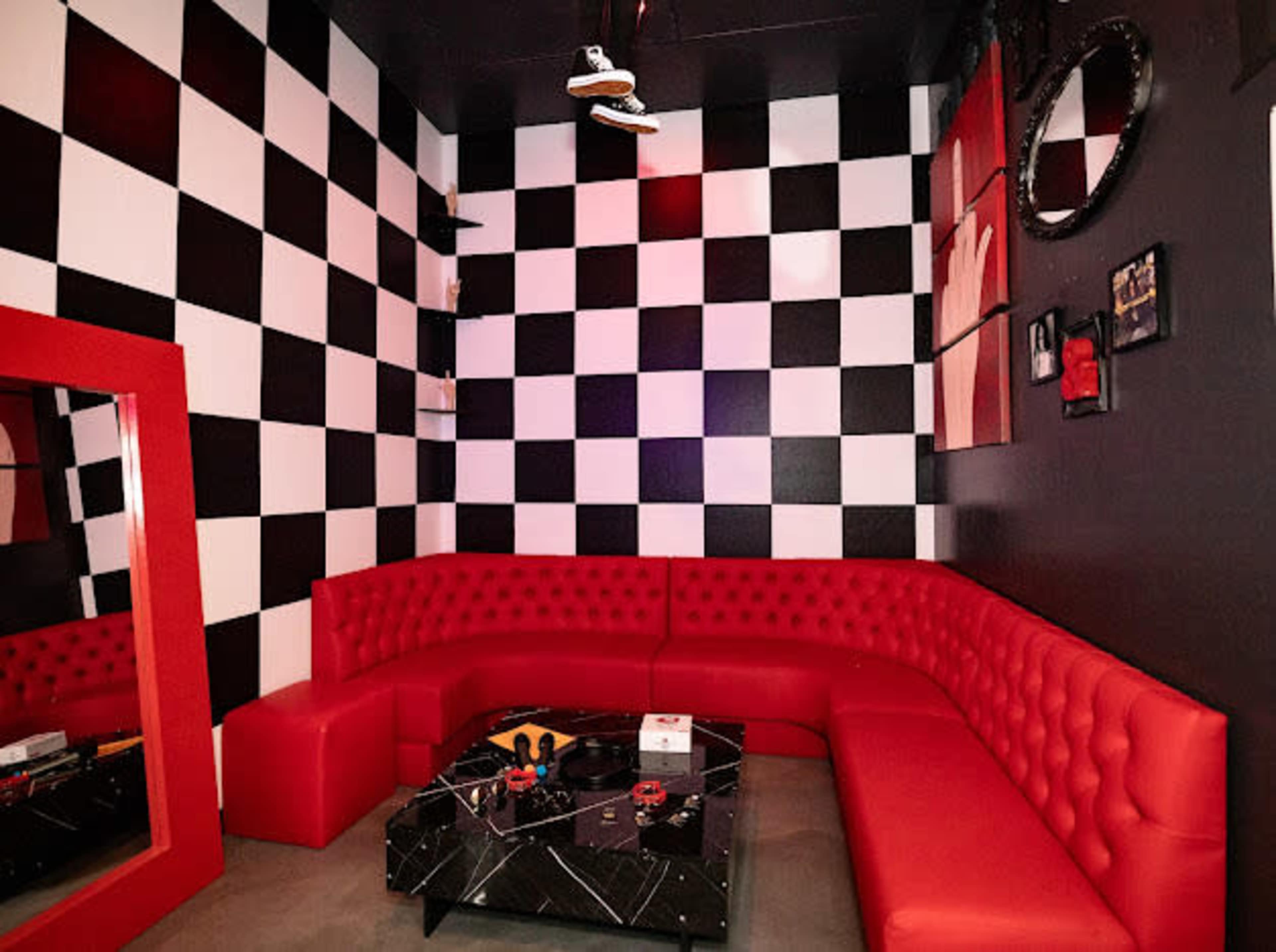 A small lounge area featuring a black and white checkered wall, a red tufted couch in a U-shape, and a black glass coffee table.