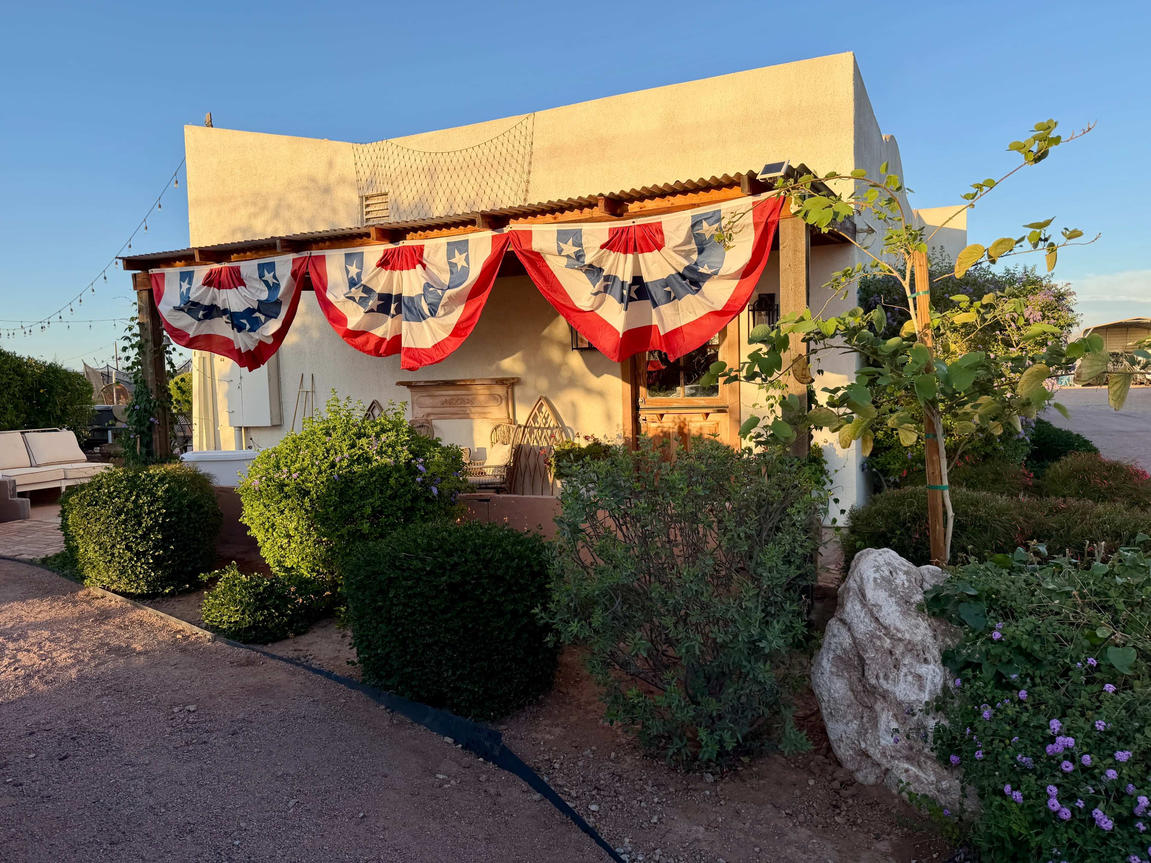 The image shows a building decorated with red, white, and blue bunting, surrounded by shrubs and plants.